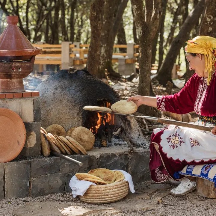 Une femme en tenue traditionnelle cuit des galettes sur un feu de bois en plein air