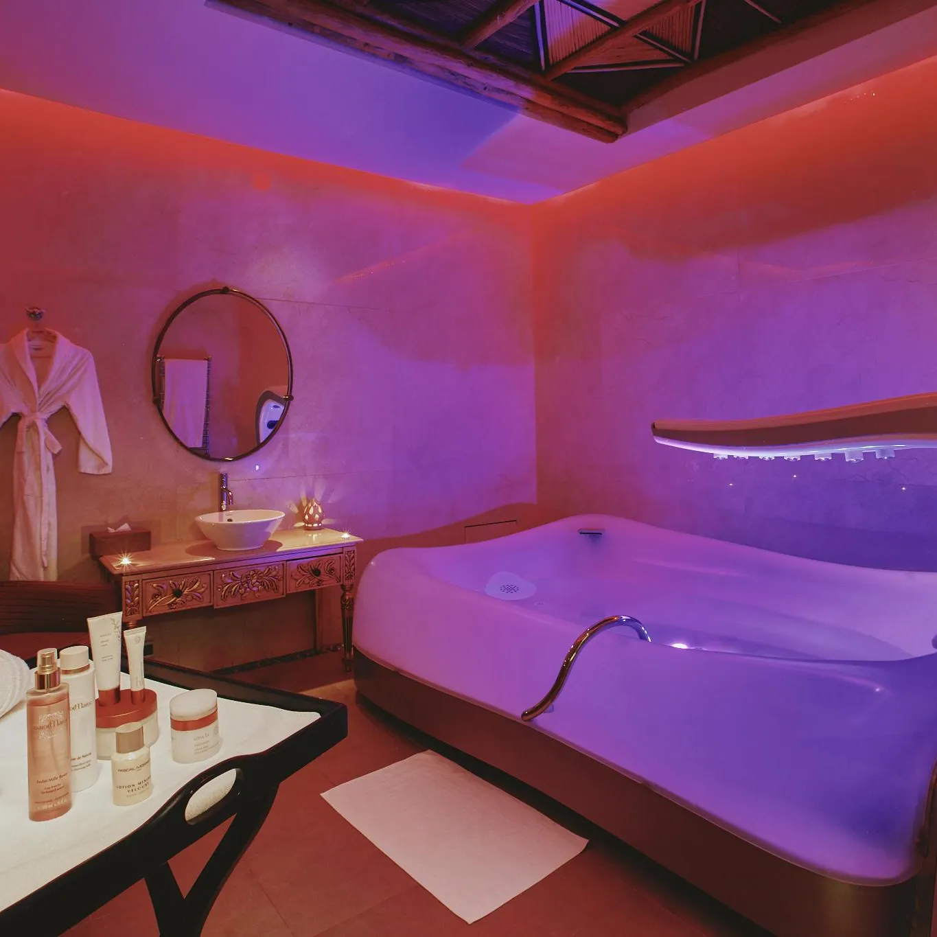 Salle de spa avec une baignoire de relaxation, un lavabo, des produits cosmétiques sur une table et une robe de bain accrochée au mur