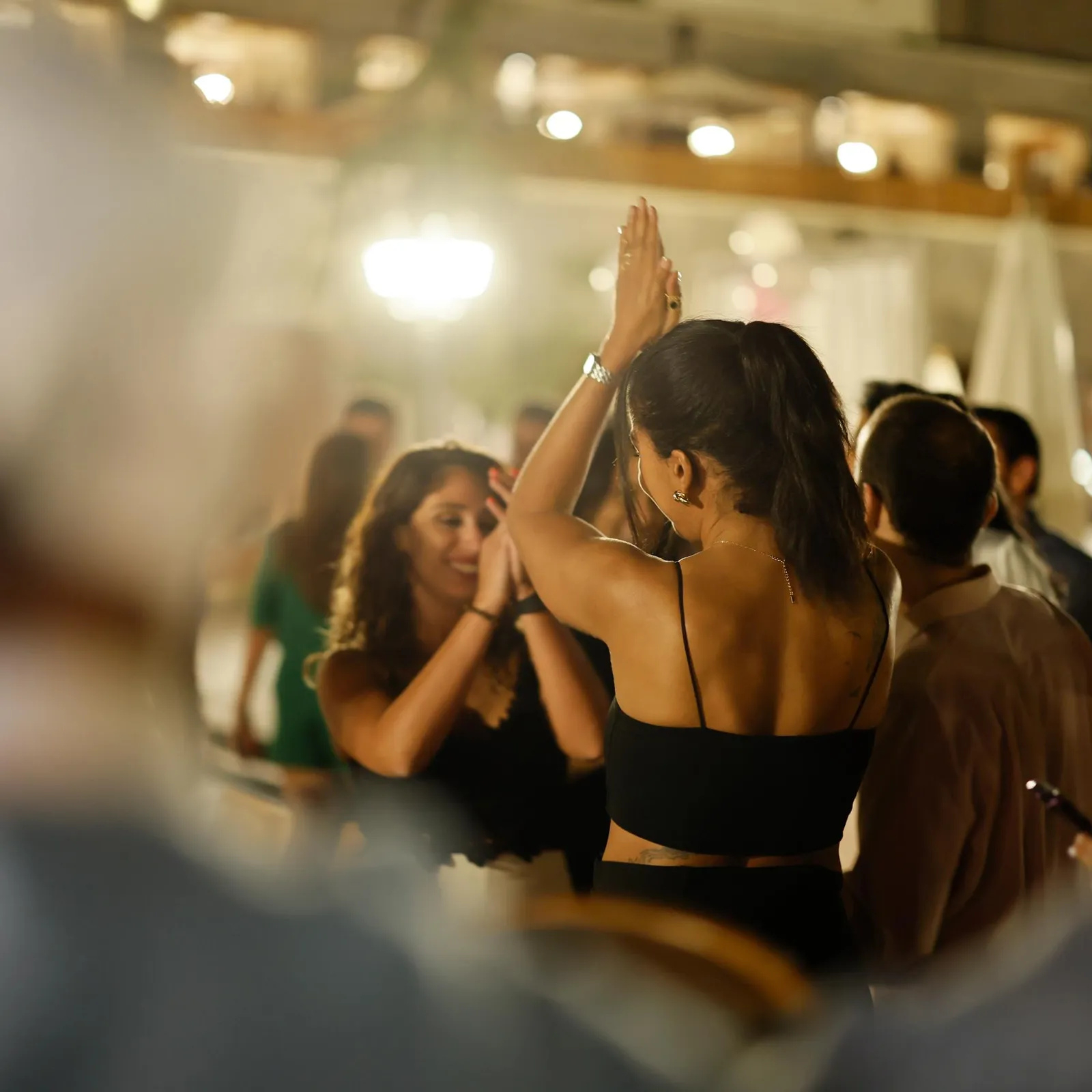 Deux femmes dansent ensemble dans une salle éclairée, entourées d'autres personnes en train de socialiser