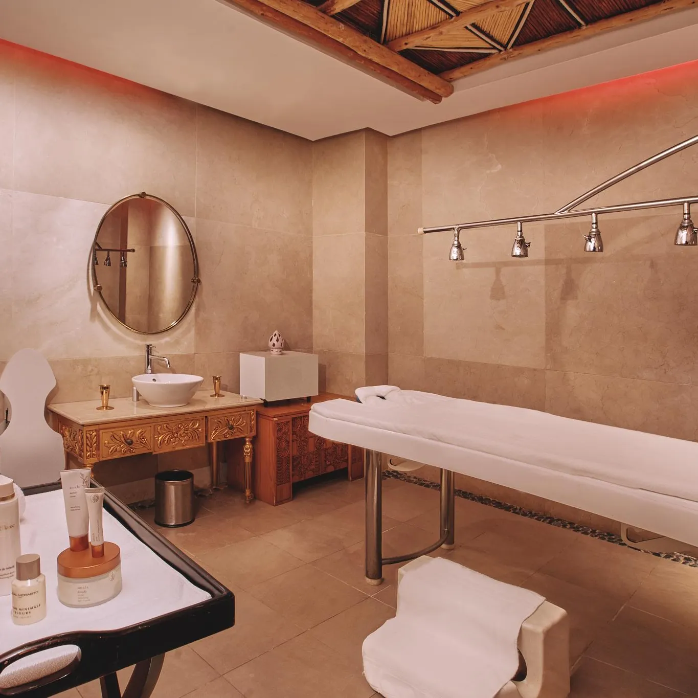 Salle de soins avec table de massage, miroir, lavabo et produits cosmétiques sur une table