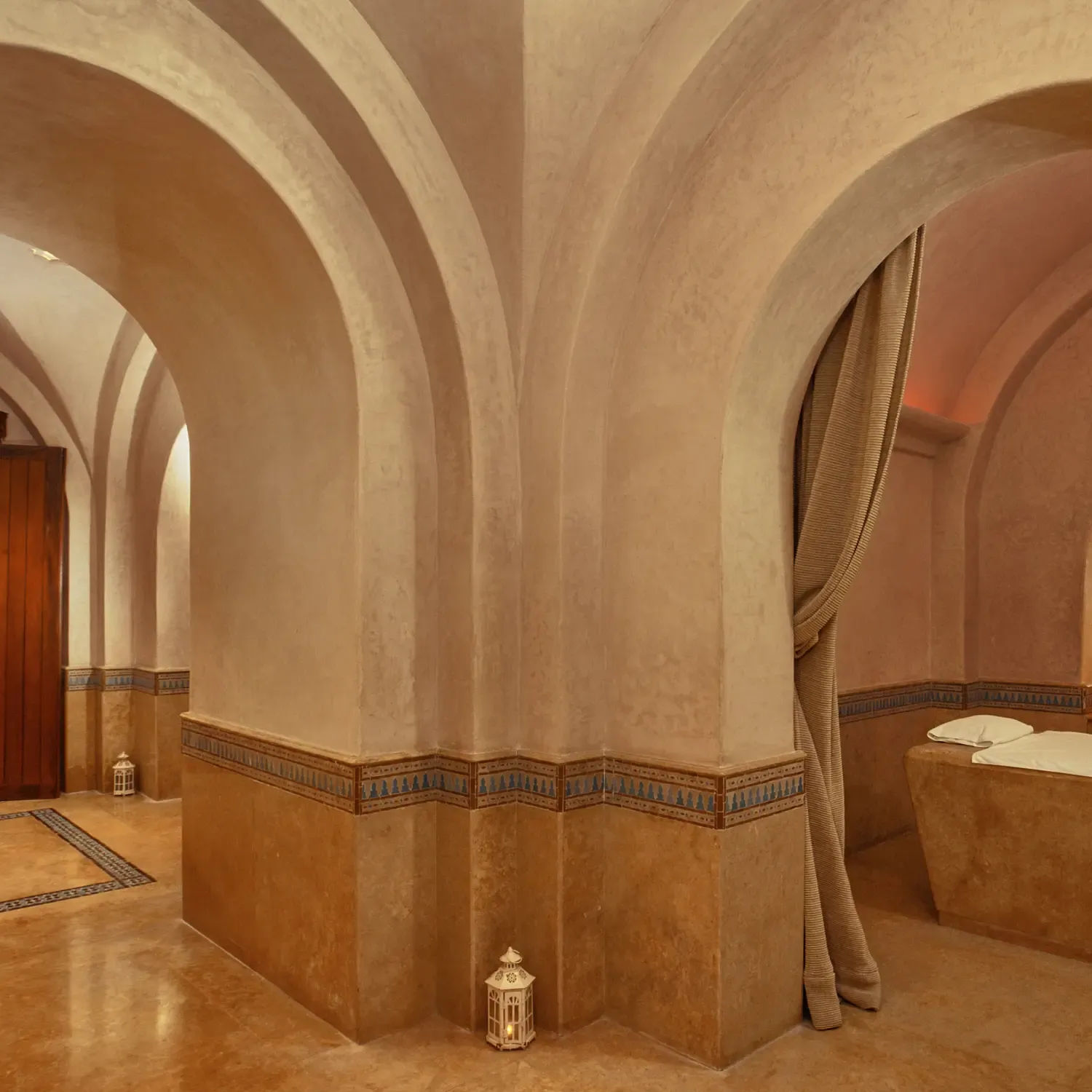 Salle de bain luxueuse avec arches, carrelage beige et motifs décoratifs, contenant des lavabos et une baignoire