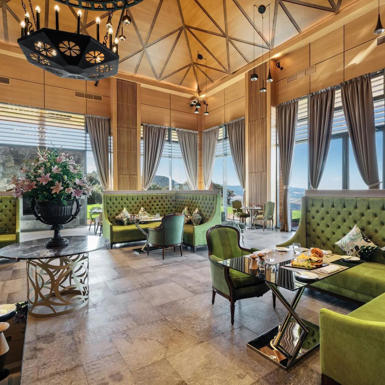 Un restaurant élégant avec des banquettes vertes, des tables dressées et de grandes fenêtres offrant une vue panoramique