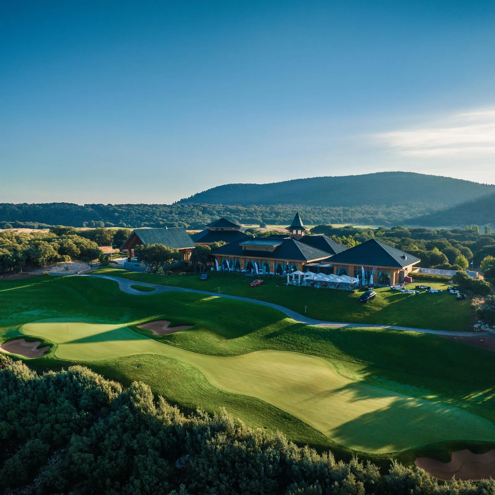 Un terrain de golf avec un club-house en bois et des montagnes en arrière-plan sous un ciel dégagé