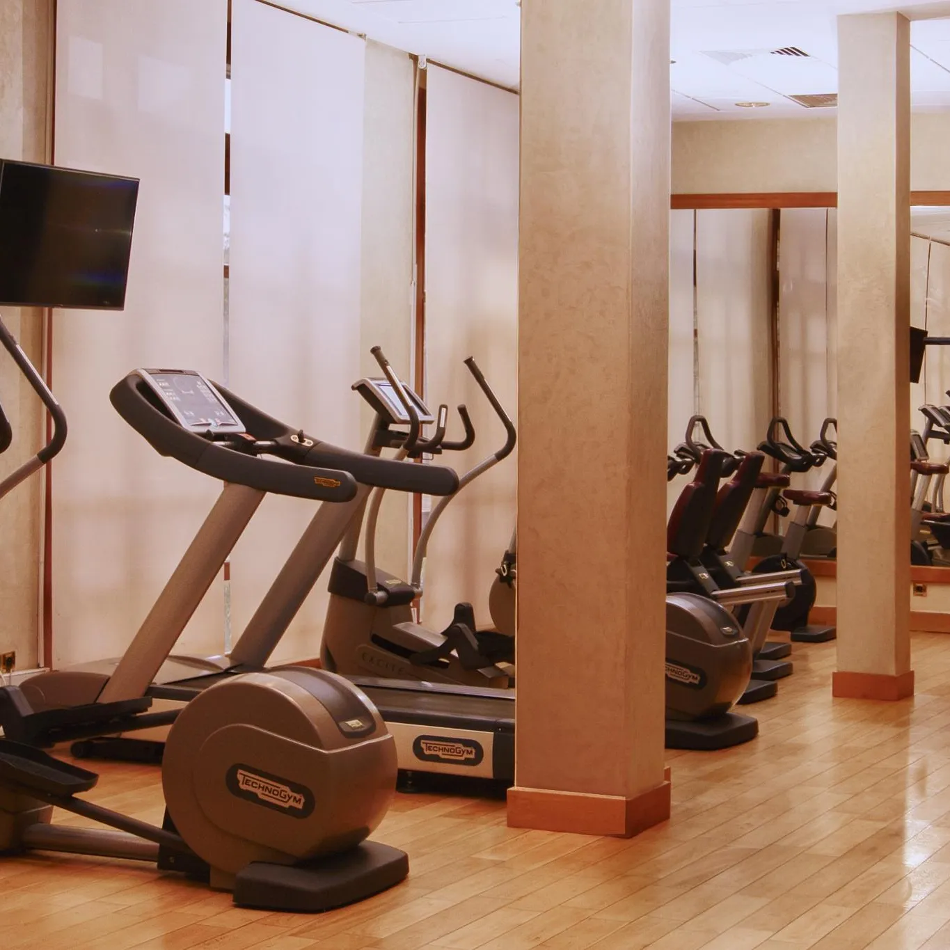 Salle de sport avec plusieurs appareils de cardio-training, dont des elliptiques et des vélos, alignés contre un mur avec des miroirs