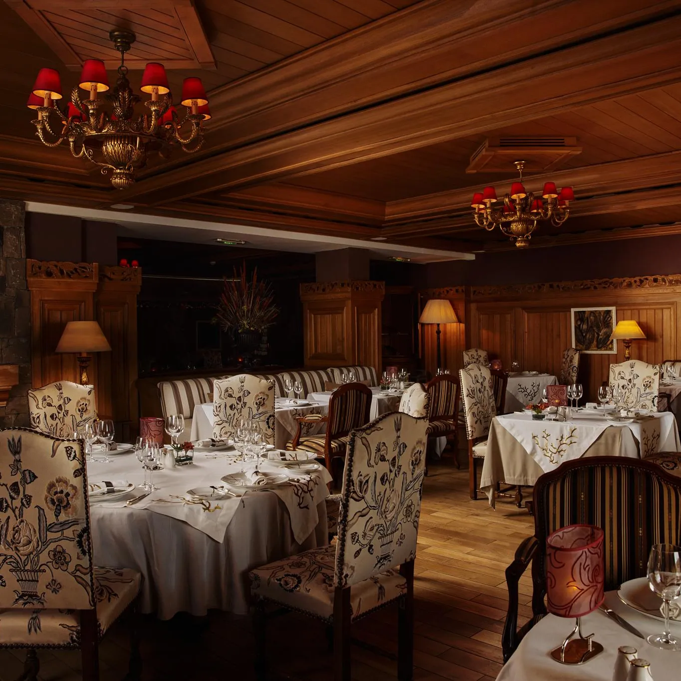 Restaurant élégant avec des tables dressées, des chandeliers et des chaises à motifs floraux, éclairé par des lampes et des lustres
