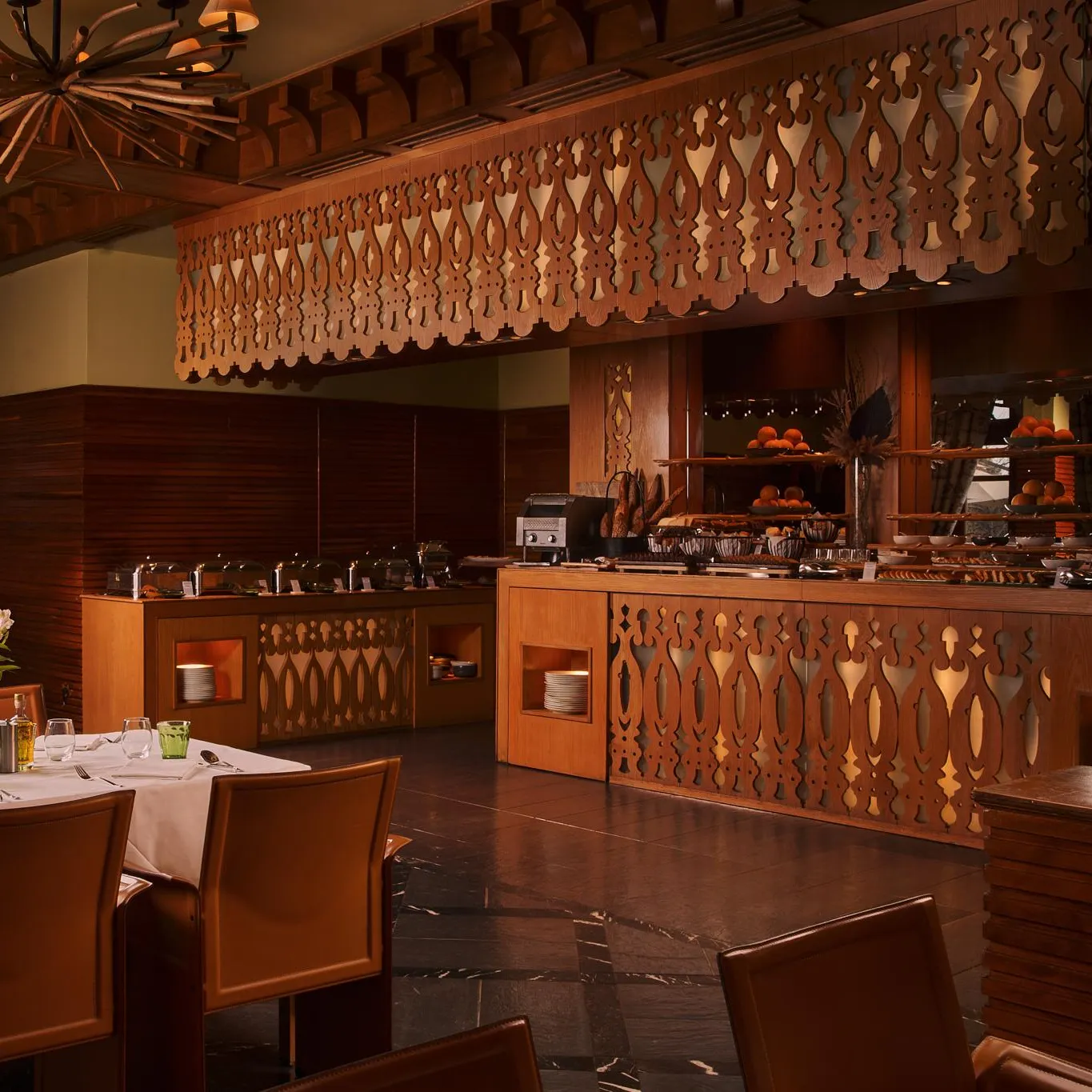Restaurant avec des tables dressées et un buffet de pâtisseries, décoré de bois et éclairé par des lampes suspendues