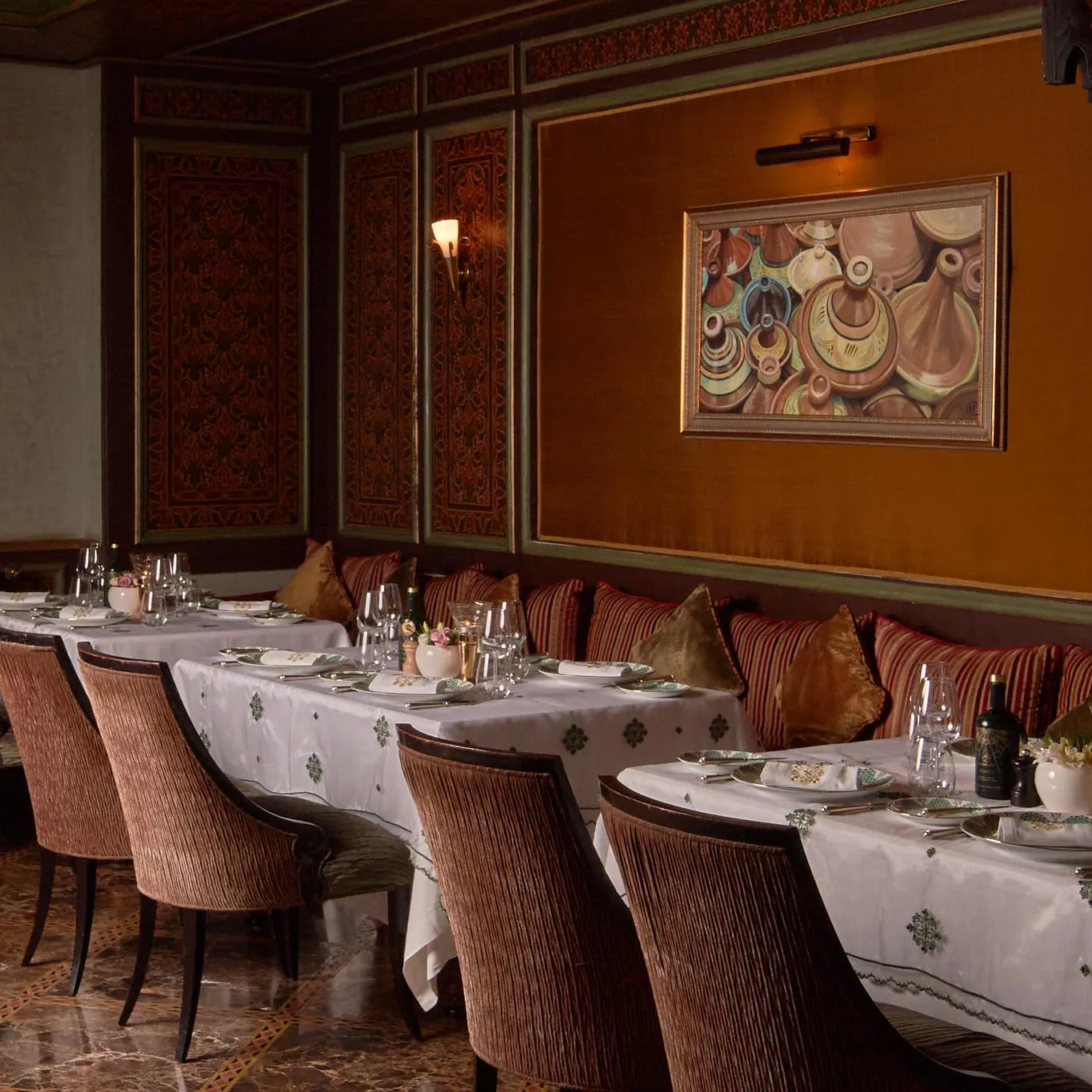 Une salle à manger élégante avec des tables dressées et des chaises rembourrées, décorée de coussins et d'un tableau mural coloré
