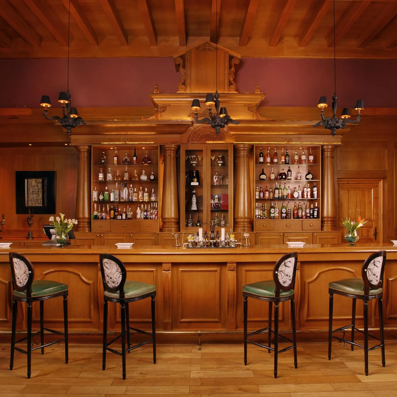 Un bar en bois avec des étagères remplies de bouteilles, des tabourets verts et des fleurs sur le comptoir