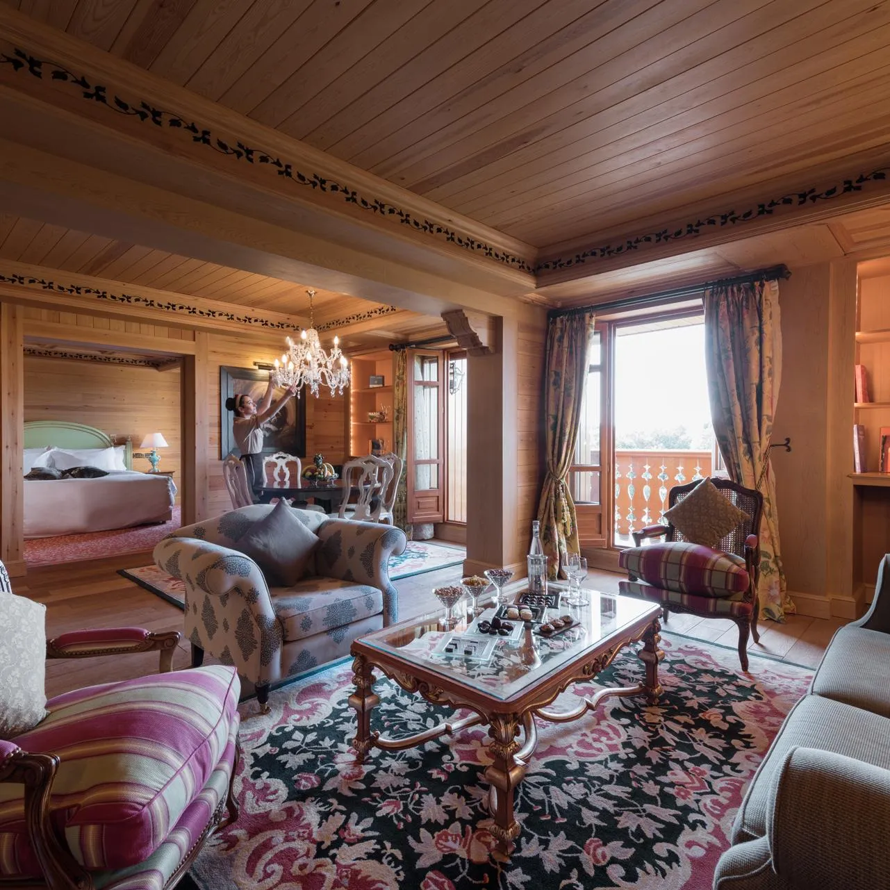 Chambre luxueuse en bois avec un coin salon, une table basse, des chaises rembourrées et un lit visible à l'arrière-plan