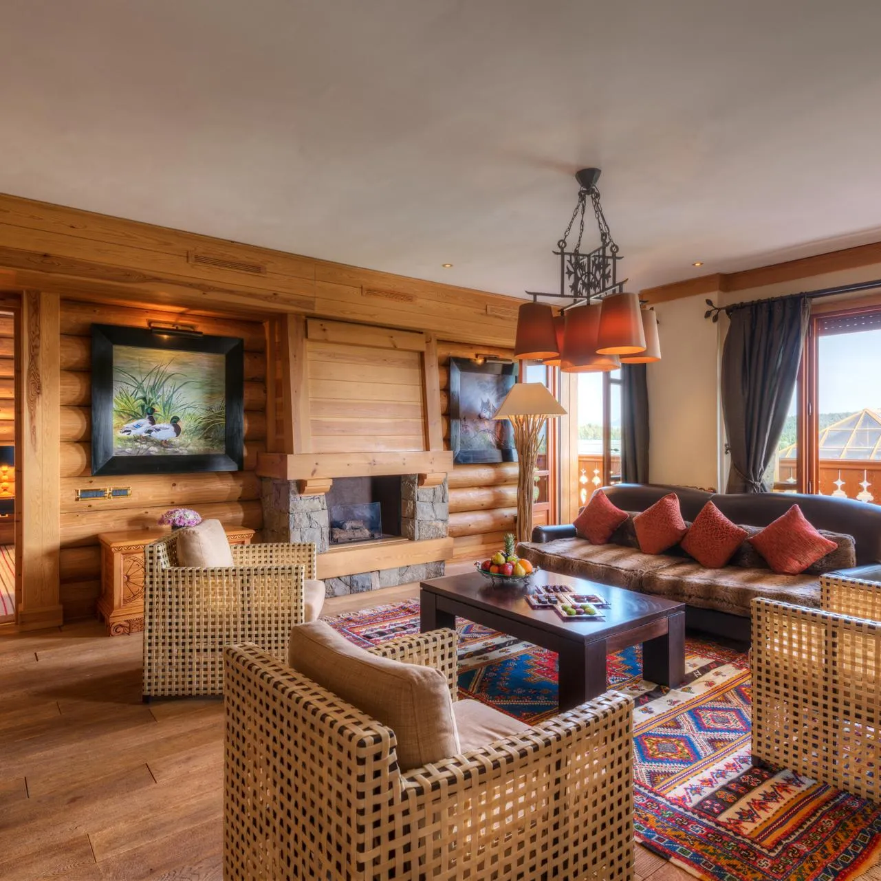 Salon en bois avec canapé, fauteuils en rotin, table basse, cheminée et grande fenêtre