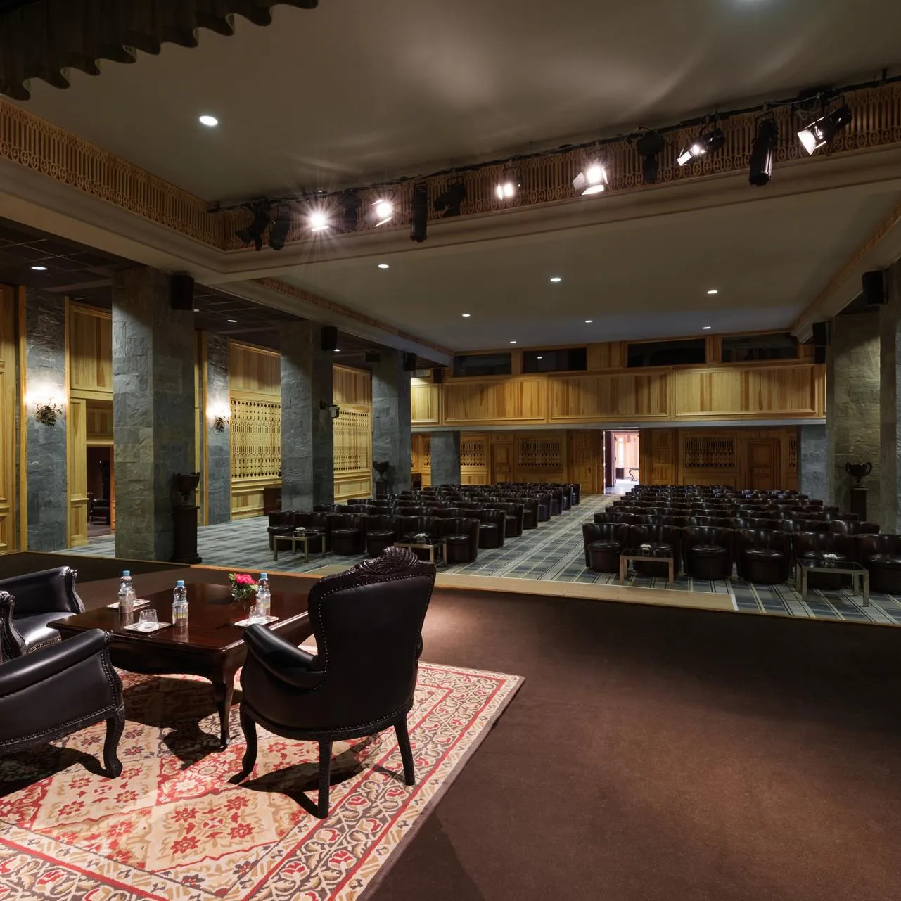 Salle de conférence avec des rangées de chaises et un espace lounge avec deux fauteuils et une table basse