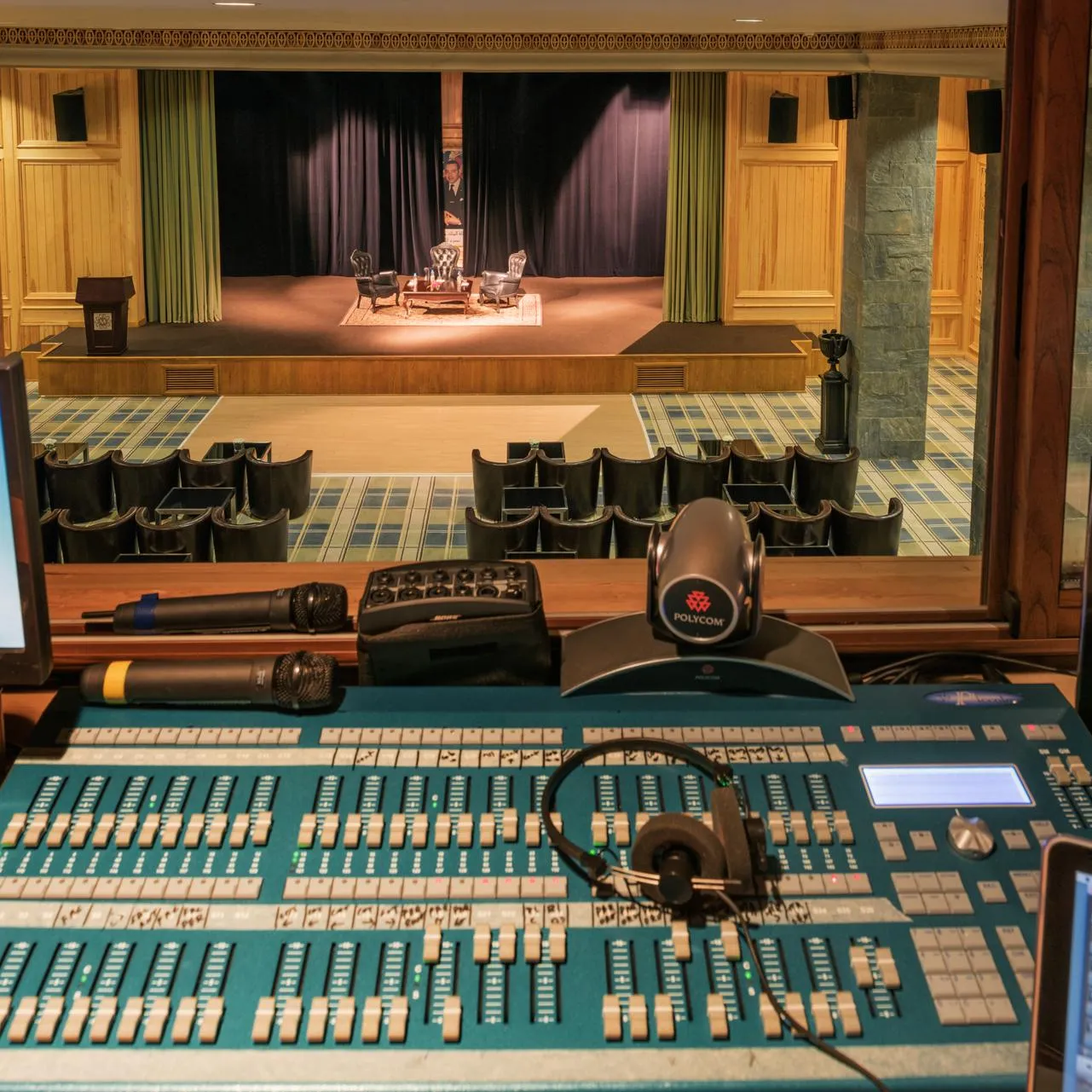 Table de mixage audio avec écrans et microphones devant une scène de théâtre avec des chaises et un rideau fermé