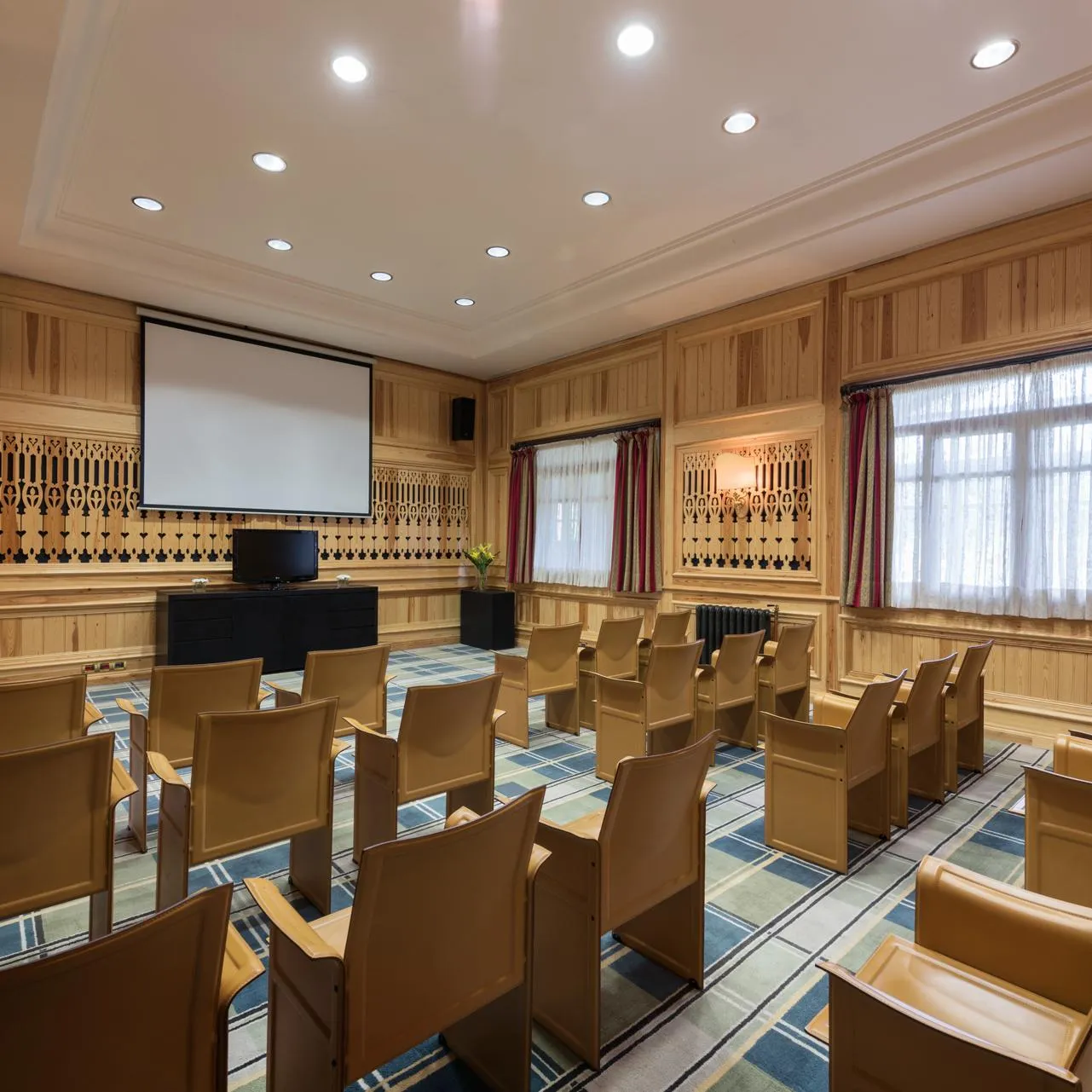 Salle de réunion avec des chaises en bois, un écran de projection, un projecteur et des fenêtres avec des rideaux