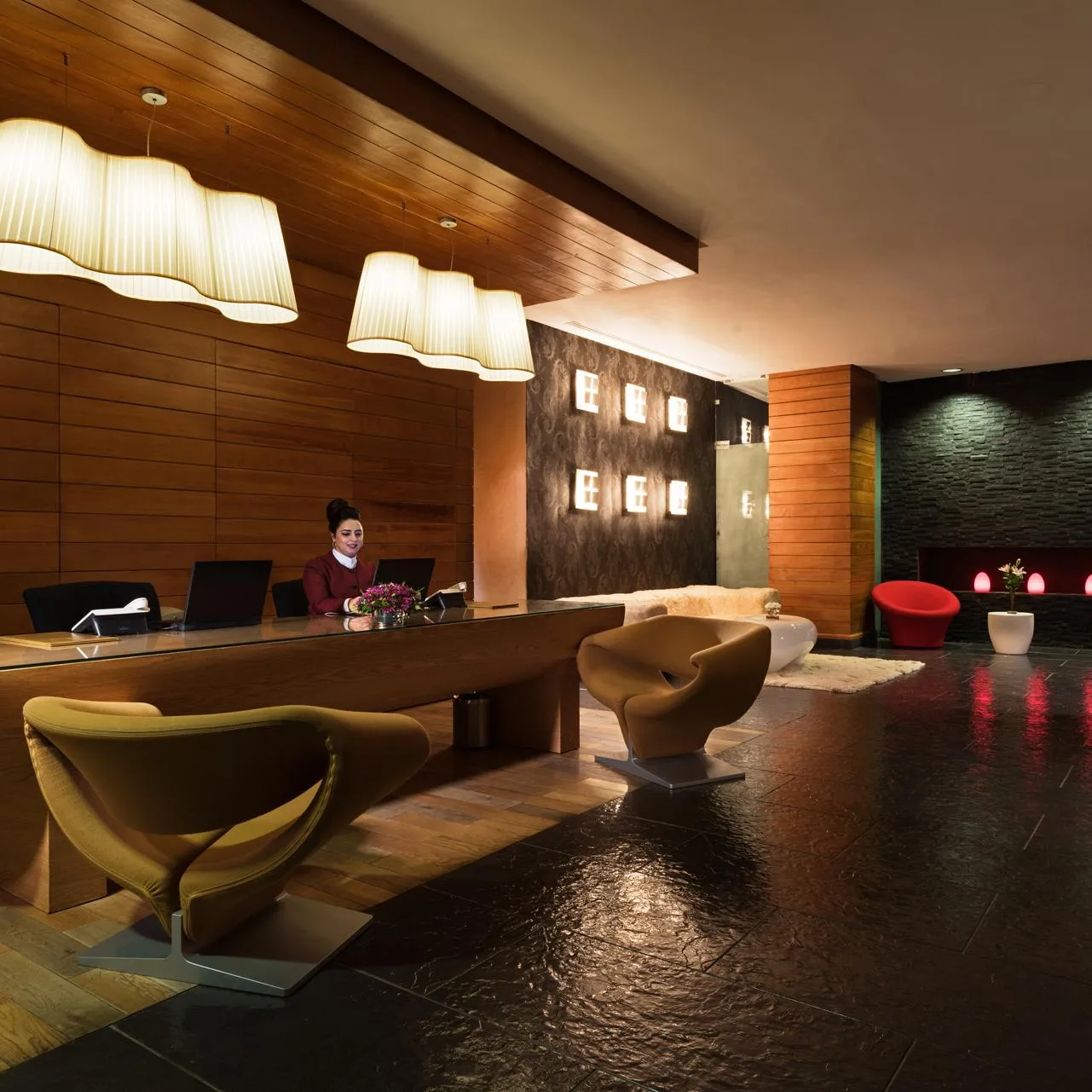 Réception d'hôtel moderne avec un comptoir de réception en verre, des sièges colorés et des luminaires suspendus