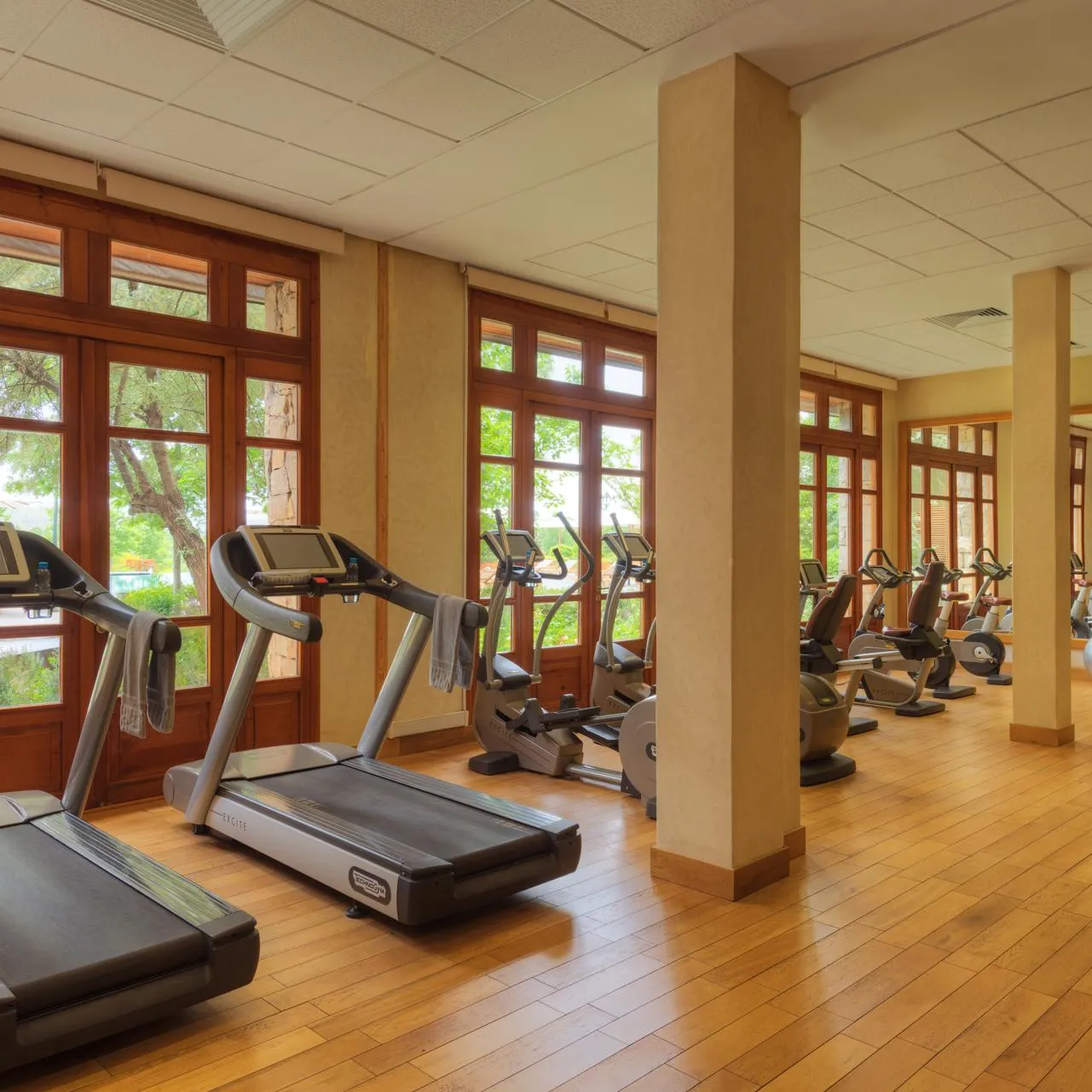Salle de sport avec plusieurs tapis de course et vélos d'exercice devant de grandes fenêtres en bois