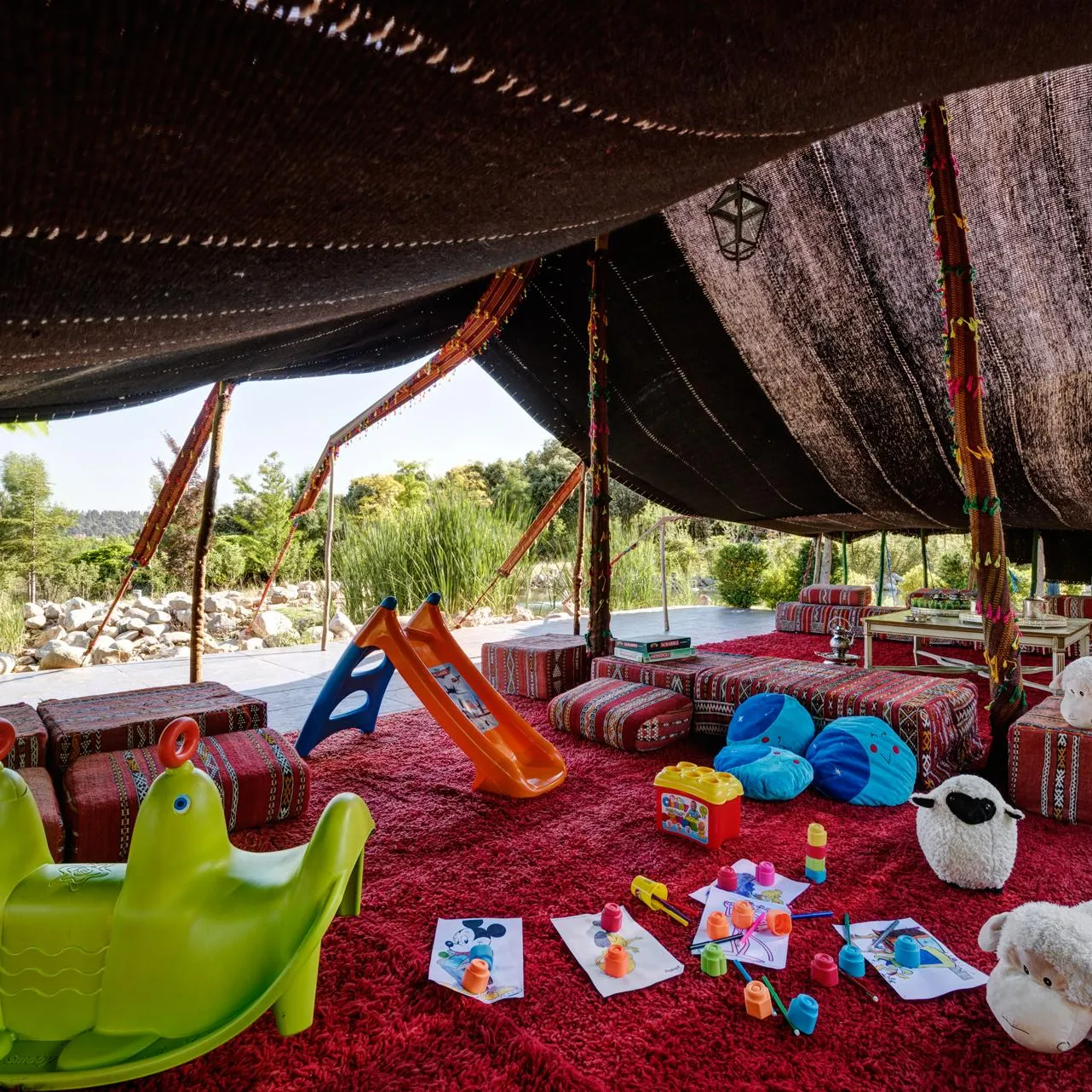 Un espace couvert avec des jouets pour enfants, des coussins et des décorations colorées, entouré de végétation