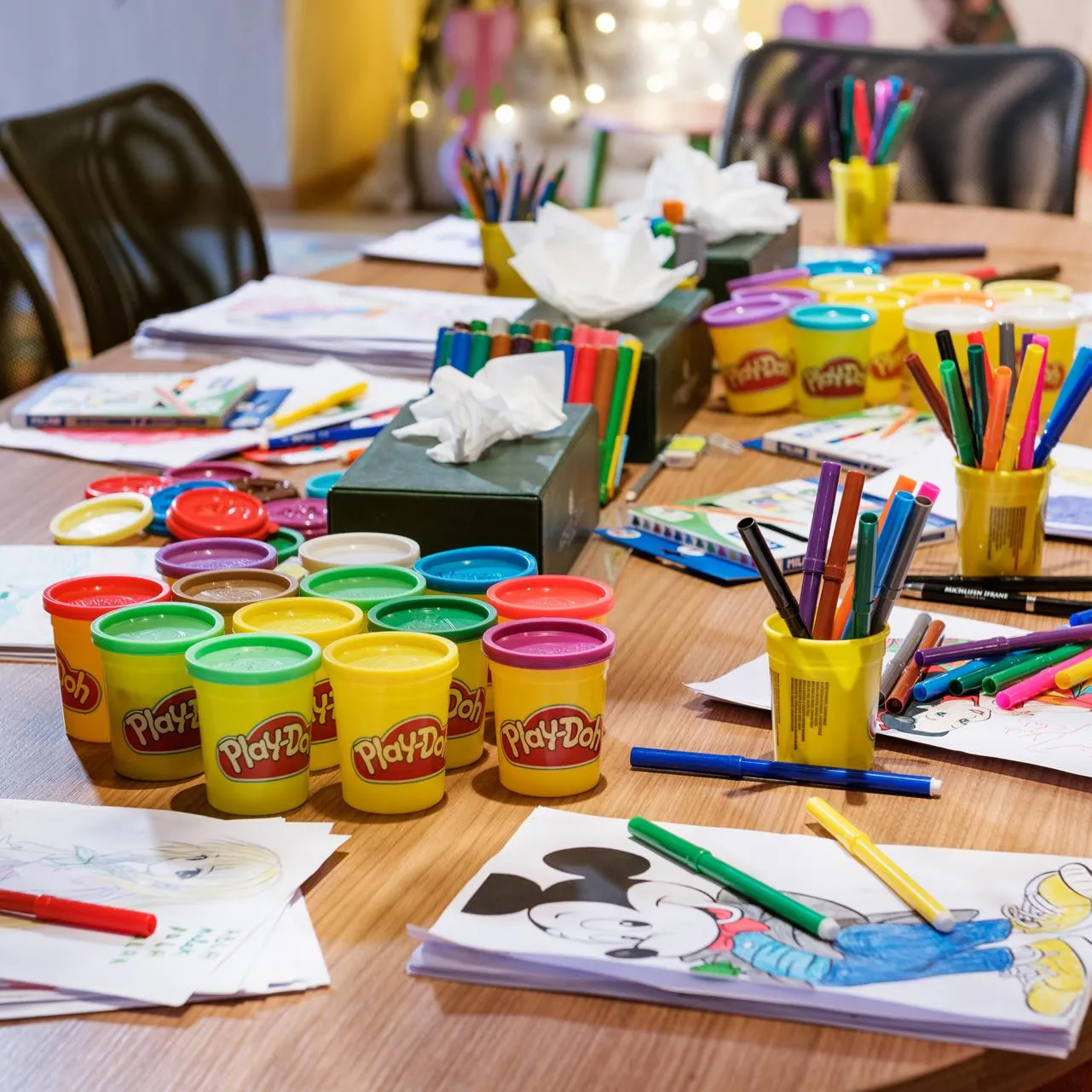Table avec du matériel de dessin, des pots de pâte à modeler Play-Doh et des feuilles colorées