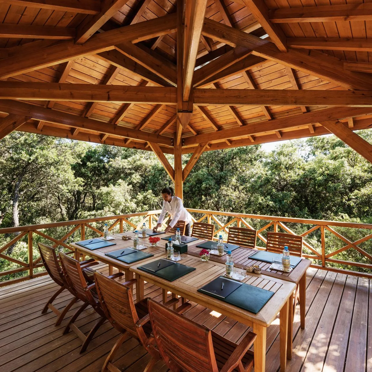 Une personne prépare des tables dans une structure en bois en plein air entourée d'arbres