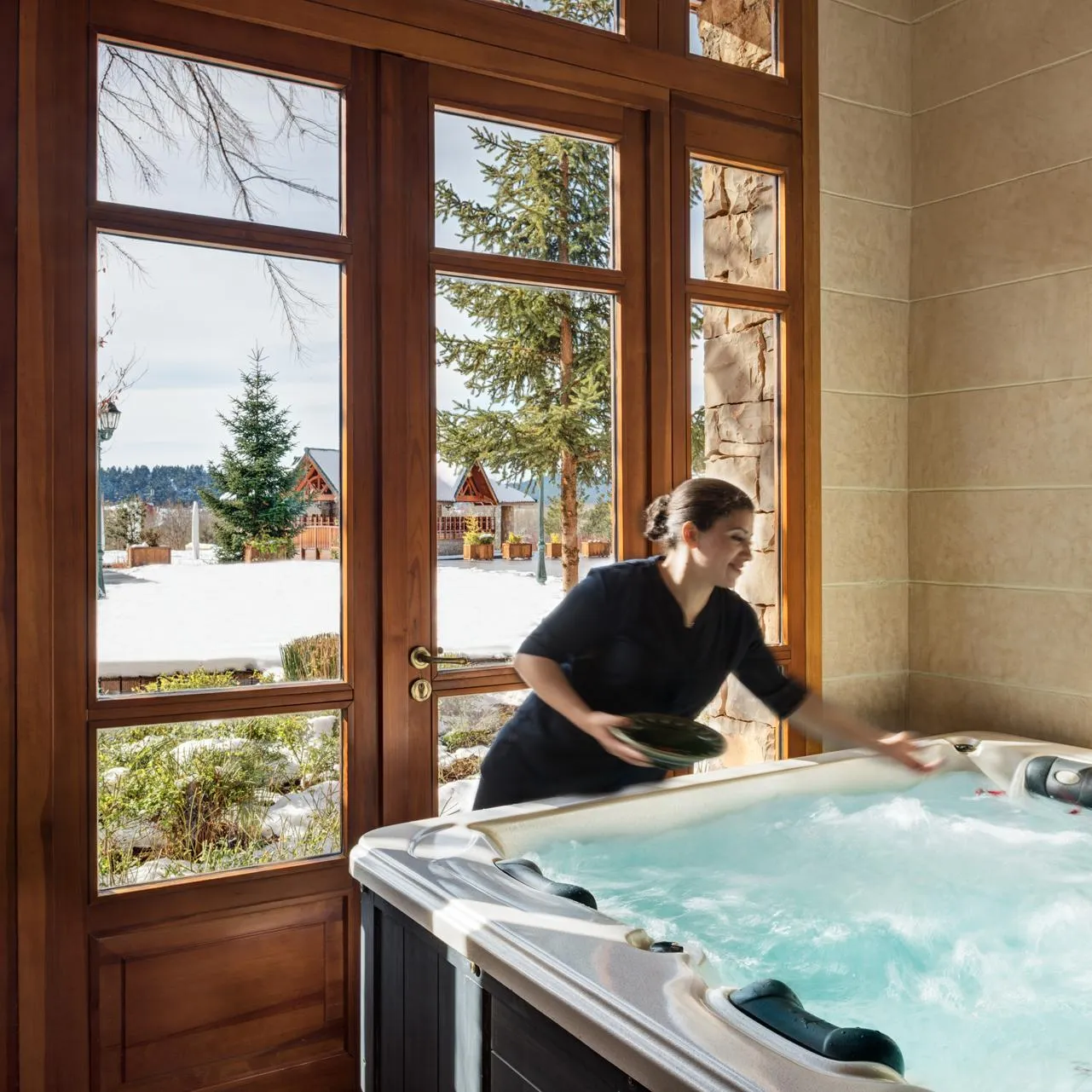 Une femme nettoie un jacuzzi dans une pièce lumineuse avec de grandes fenêtres donnant sur un paysage enneigé