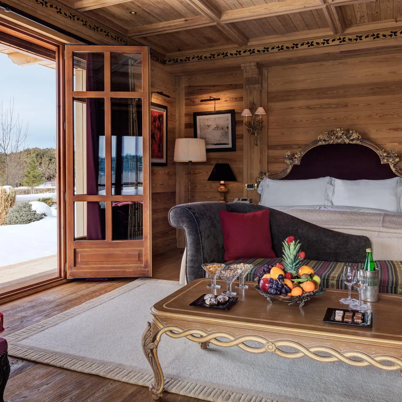 Chambre en bois avec lit à baldaquin, chaise, table basse avec fruits et verres, vue sur l'extérieur enneigé