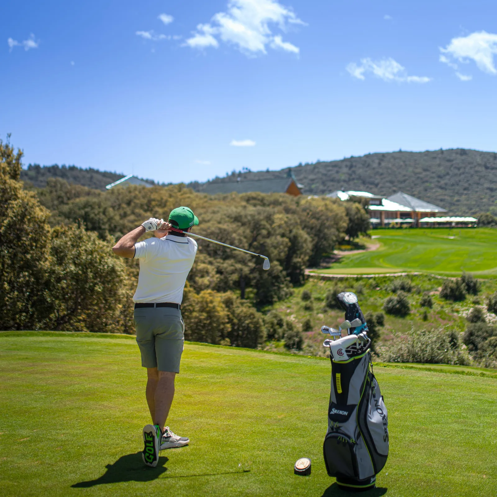 Un golfeur en train de frapper une balle sur un parcours de golf avec un sac de clubs à proximité