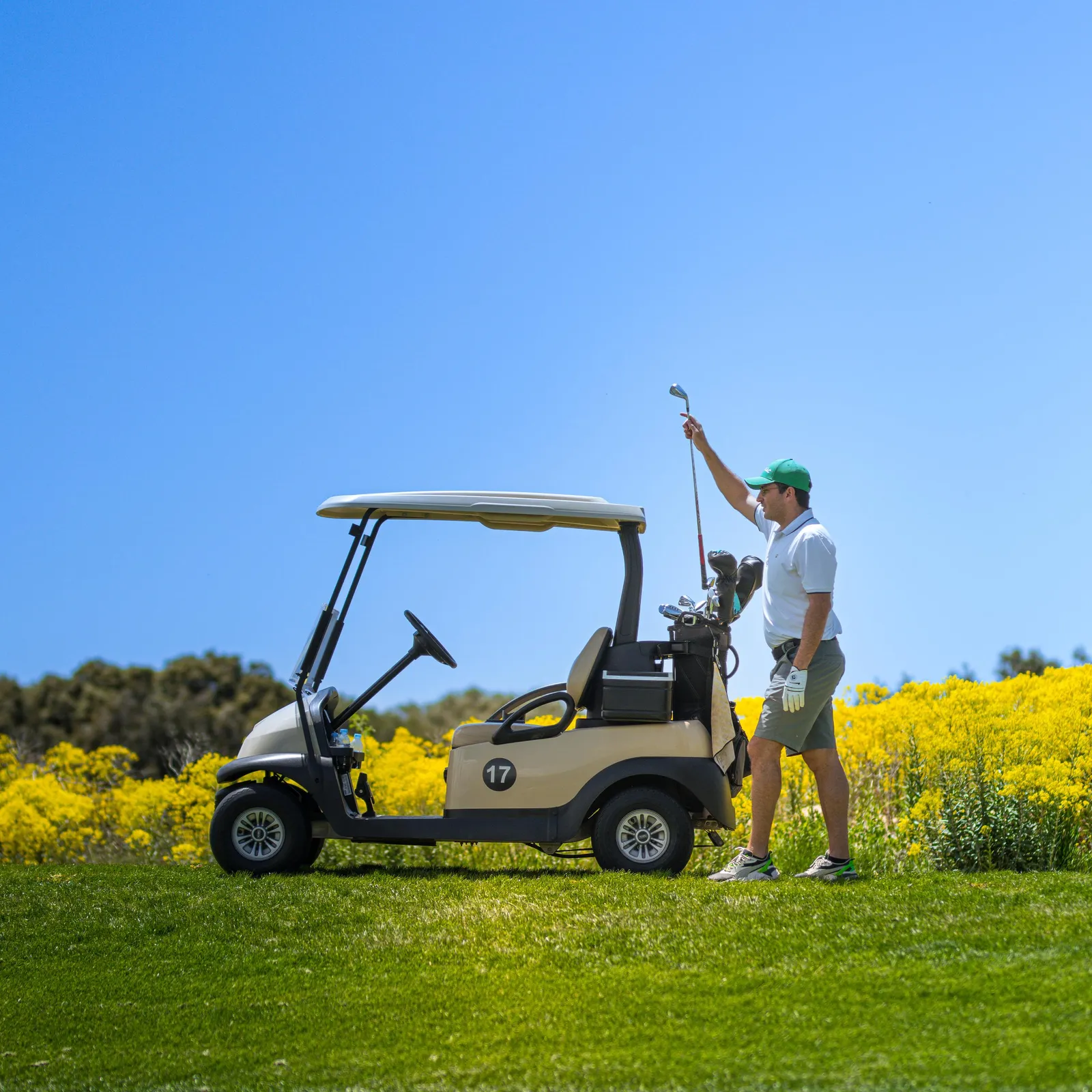 Un golfeur tient un club de golf près d'un chariot de golf sur un terrain de golf avec des fleurs jaunes en arrière-plan