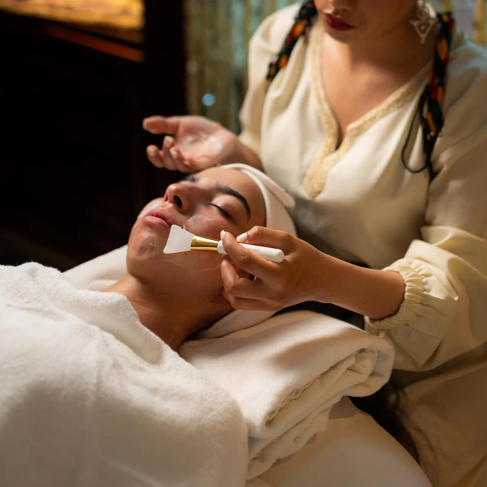 Une personne applique un masque sur le visage d'une autre personne allongée sur une serviette