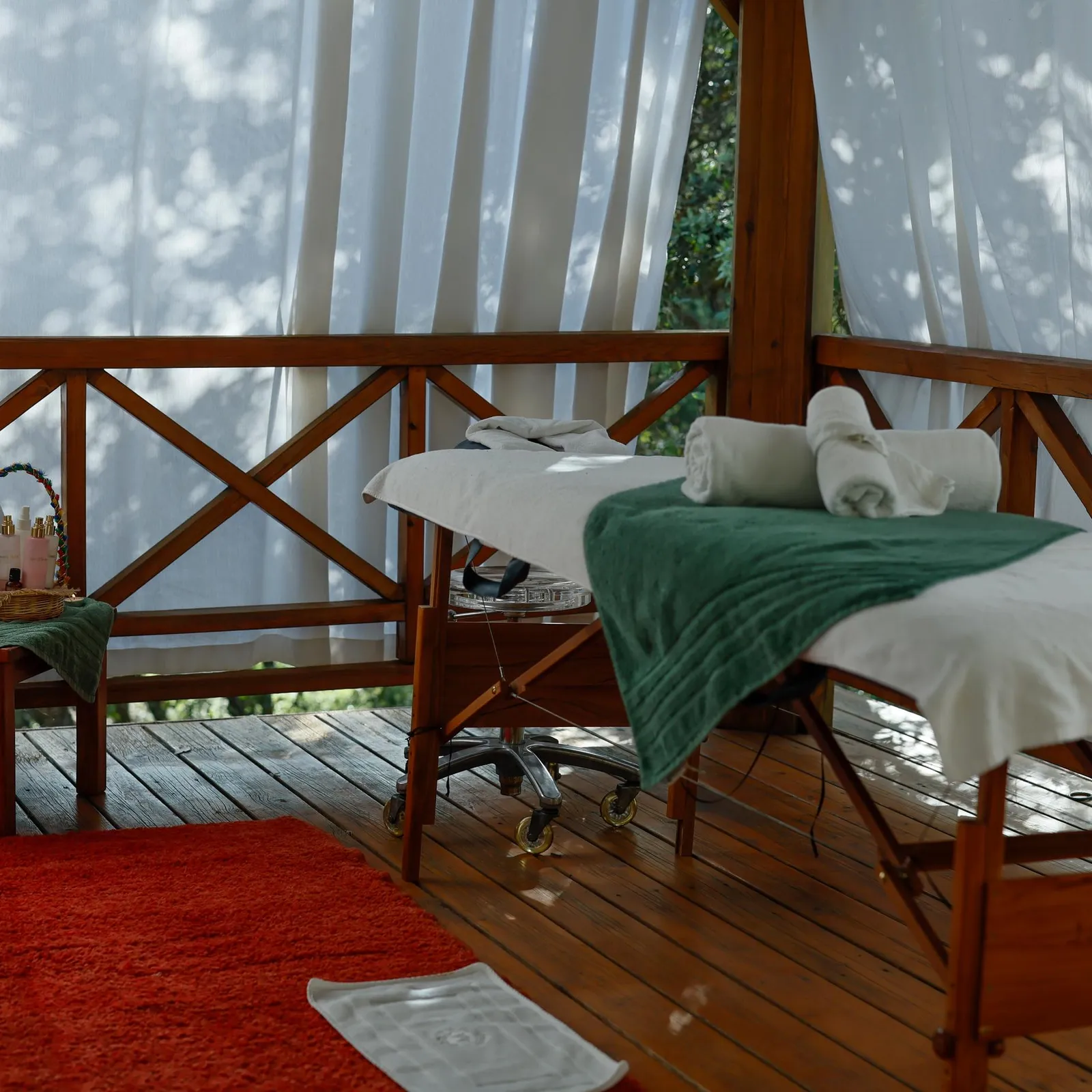 Deux tables de massage en bois avec des serviettes et des produits sur une terrasse en bois entourée de rideaux blancs