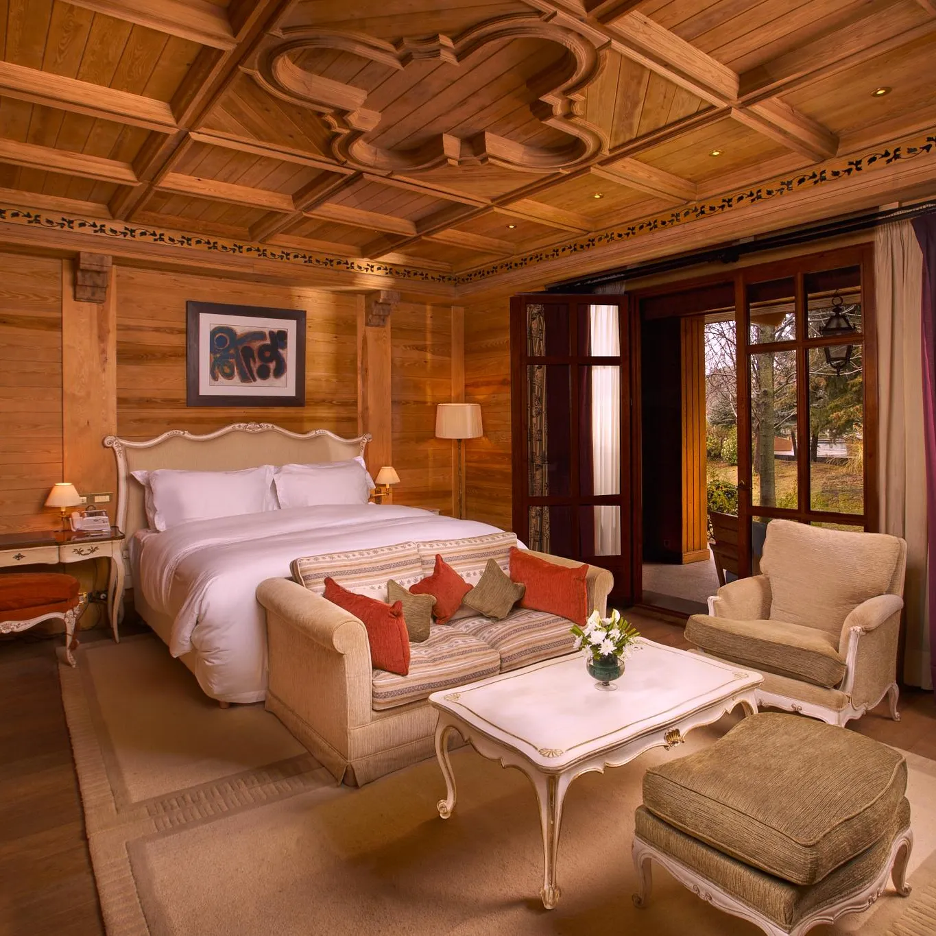 Chambre en bois avec lit double, canapé, fauteuils, table basse et fenêtres donnant sur l'extérieur