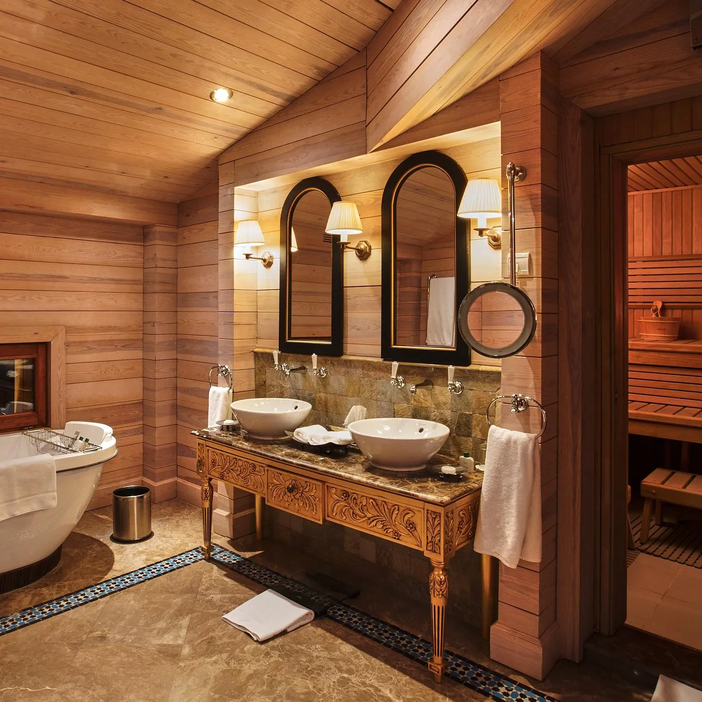 Salle de bain en bois avec baignoire, double vasque, miroir et porte ouverte sur un sauna