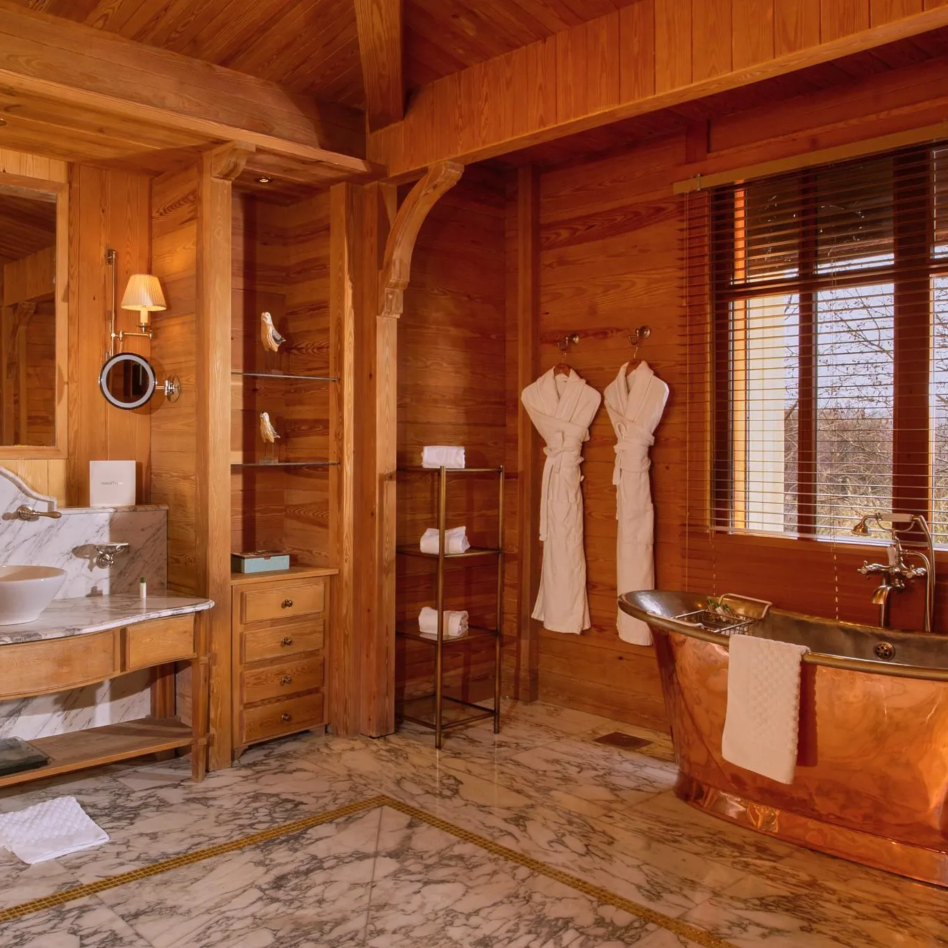 Salle de bain en bois avec lavabo en marbre, baignoire en cuivre et deux peignoirs suspendus près d'une fenêtre