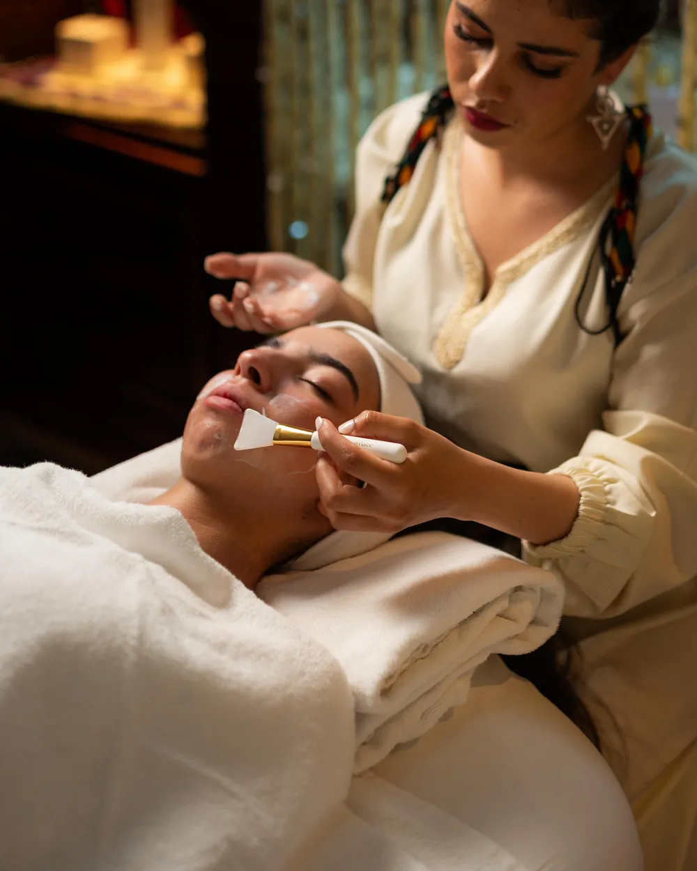 Une personne applique un masque sur le visage d'une autre personne allongée sur une serviette