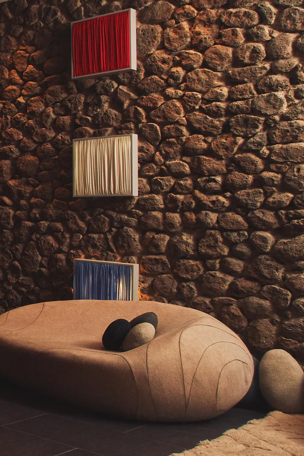 Un canapé en forme de coquillage avec des coussins est placé devant un mur en pierre avec trois cadres colorés suspendus