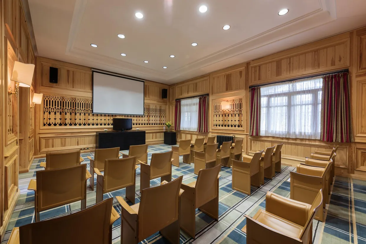 Salle de réunion avec des chaises en bois, un écran de projection, un projecteur et des fenêtres avec des rideaux