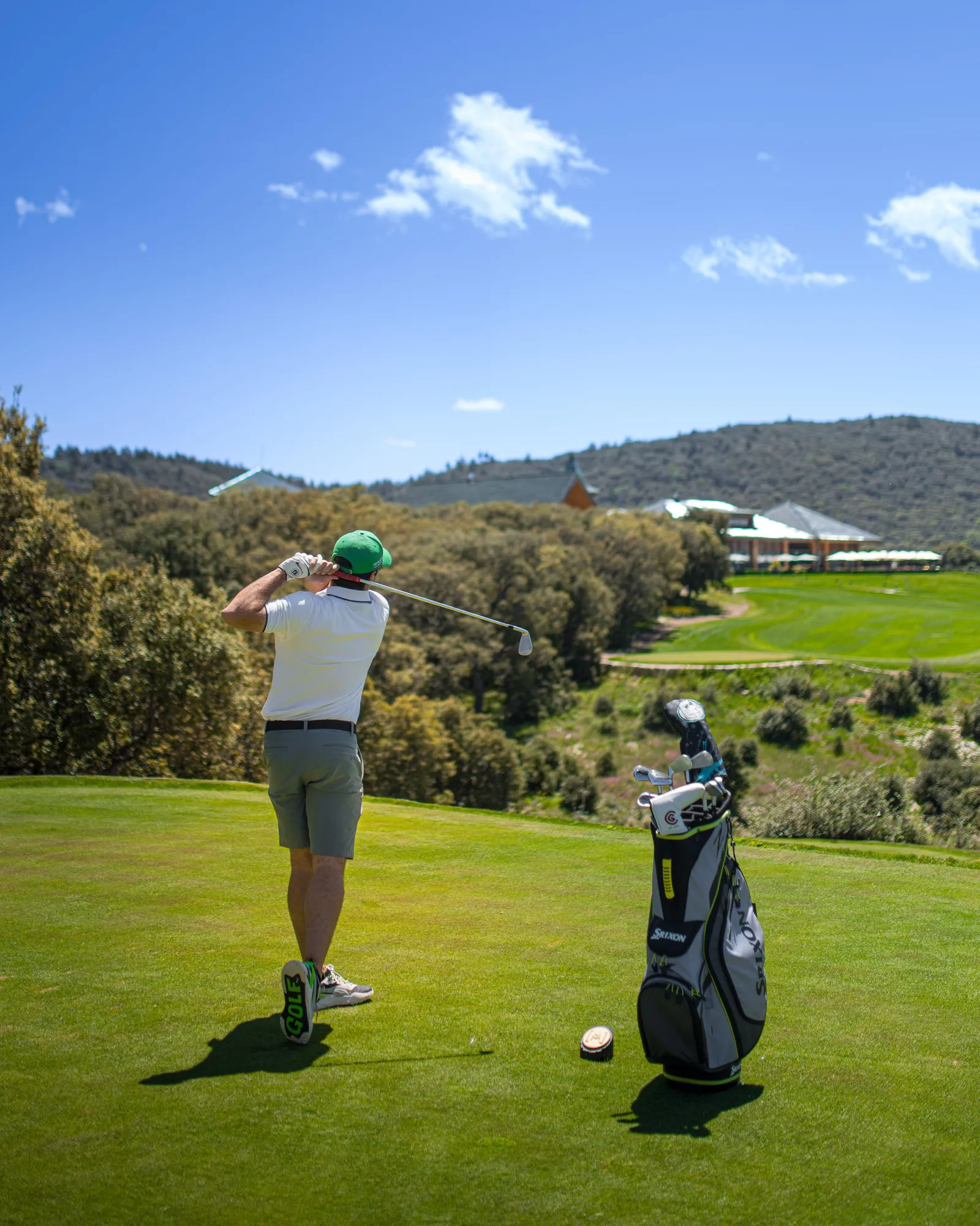 Un golfeur en train de frapper une balle sur un parcours de golf avec un sac de clubs à proximité