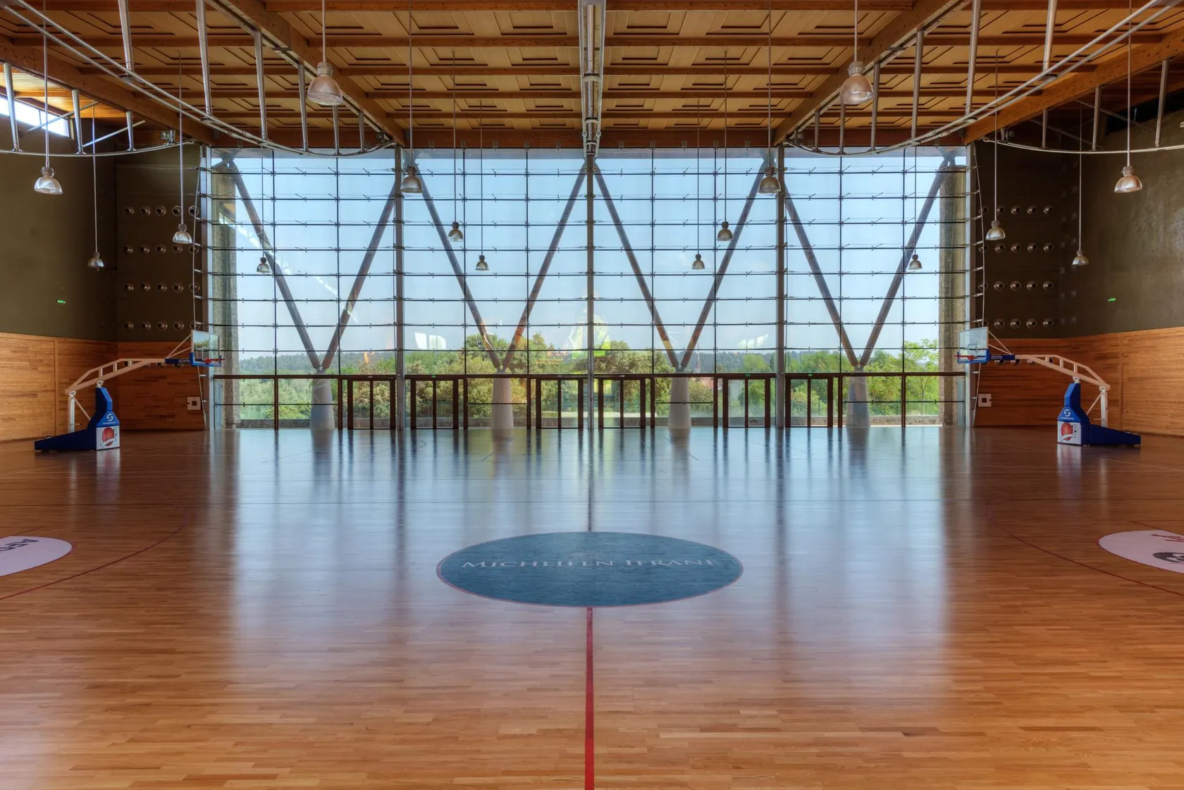 Gymnase intérieur avec un parquet poli, des panneaux de basket et une grande baie vitrée en face