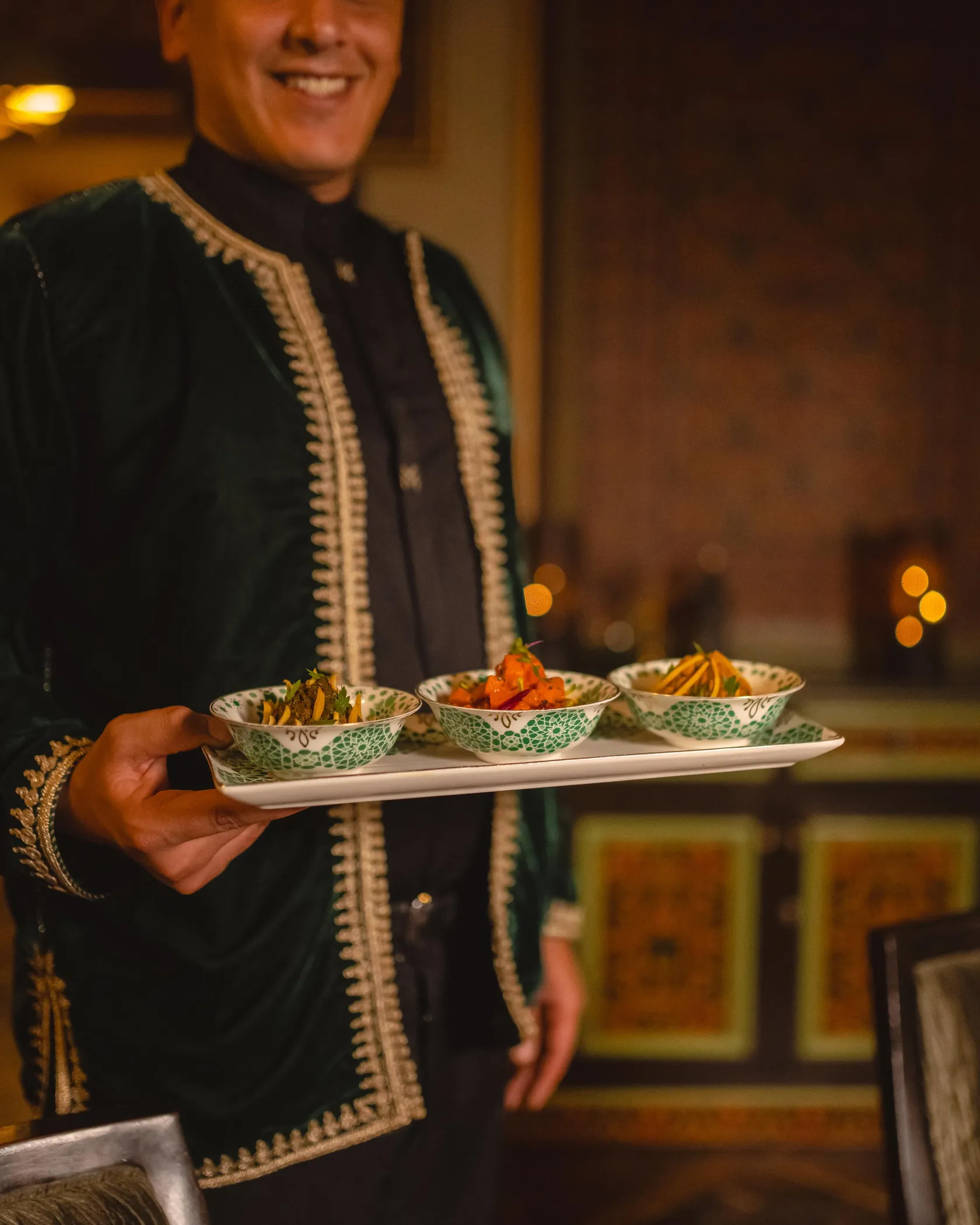 Une personne en tenue traditionnelle porte un plateau avec trois bols contenant des légumes et des garnitures