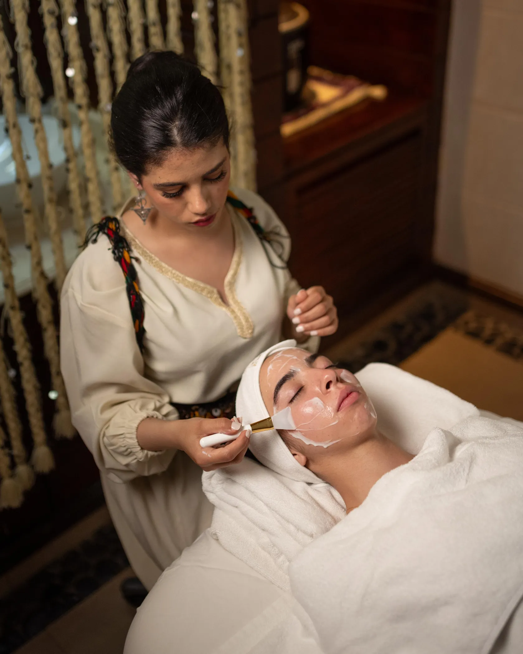 Une personne applique un masque facial à une autre personne allongée sur une serviette blanche