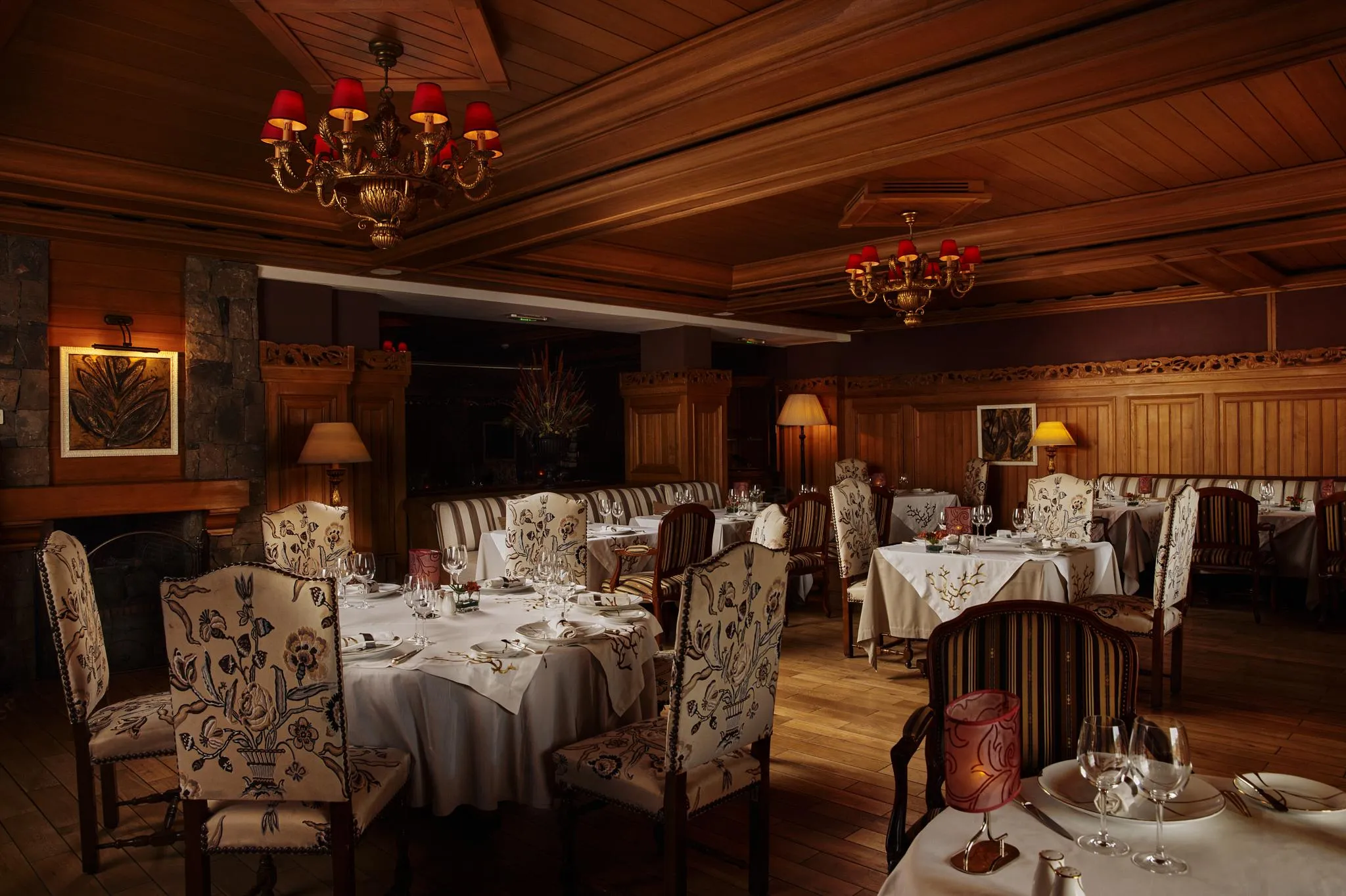 Restaurant élégant avec des tables dressées, des chandeliers et des chaises à motifs floraux, éclairé par des lampes et des lustres