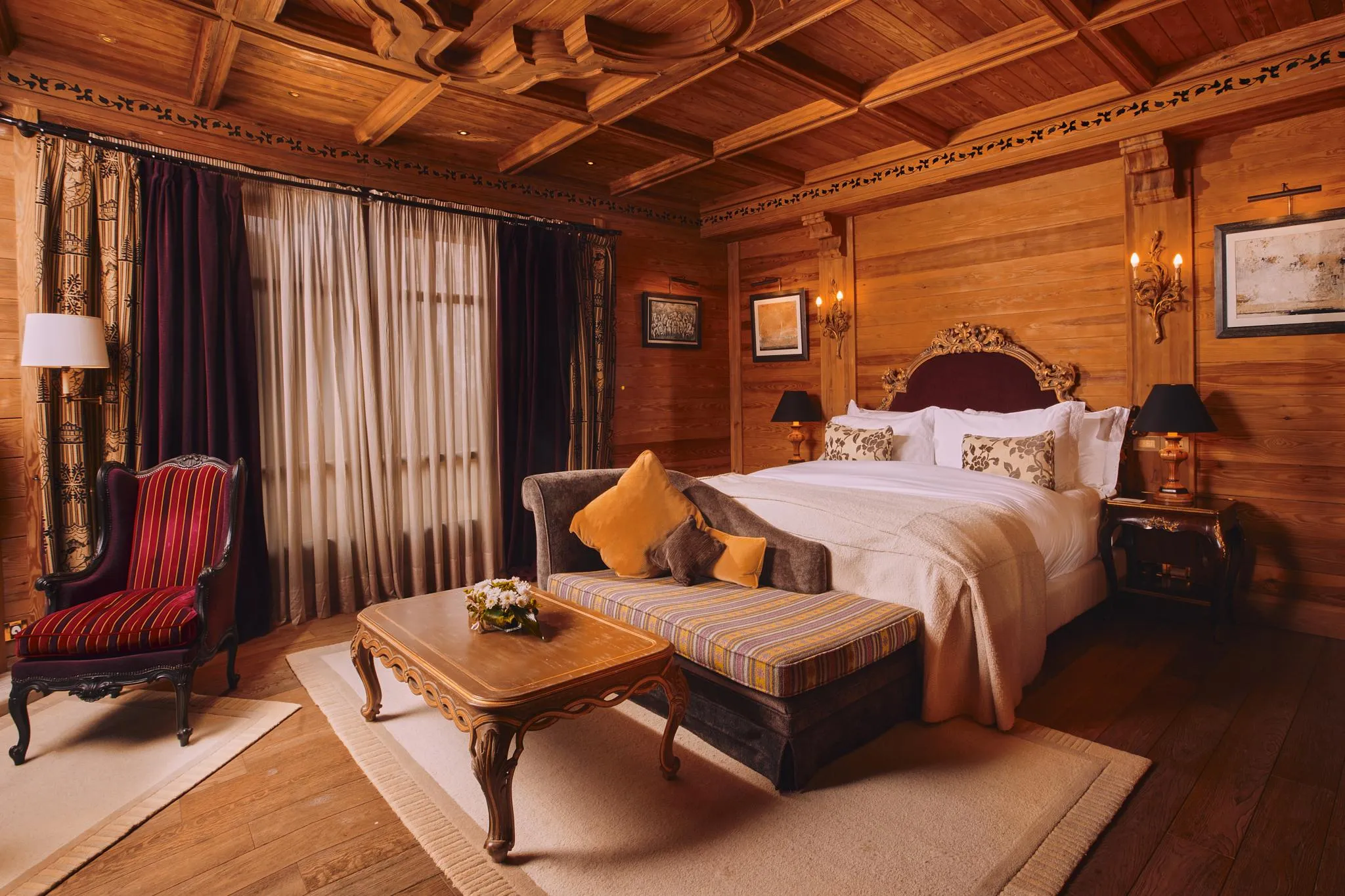 Chambre en bois avec un lit à baldaquin, une banquette, une table basse et des rideaux aux fenêtres