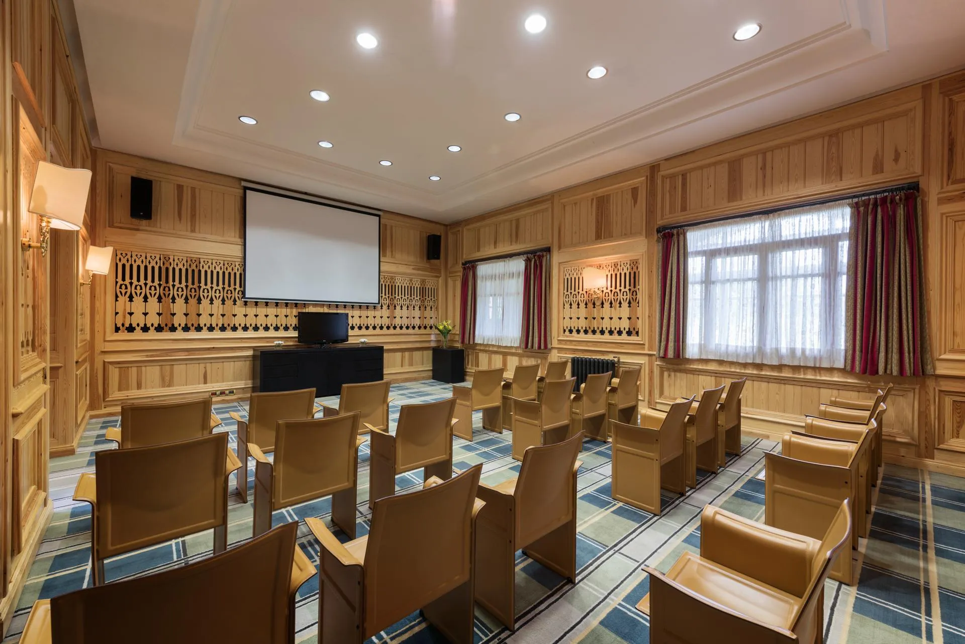 Salle de réunion avec des chaises en bois, un écran de projection, un projecteur et des fenêtres avec des rideaux