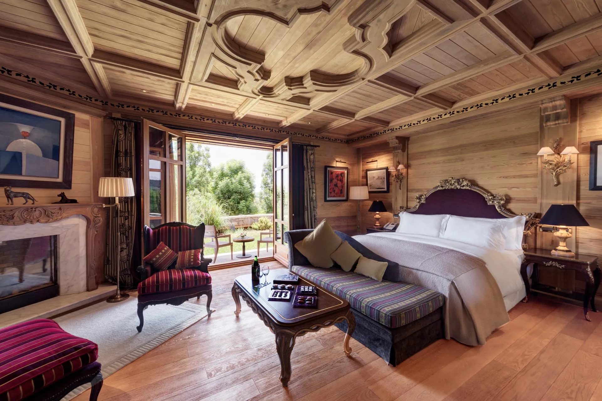 Chambre en bois avec lit, canapé, table basse, cheminée et portes-fenêtres ouvrant sur une terrasse extérieure