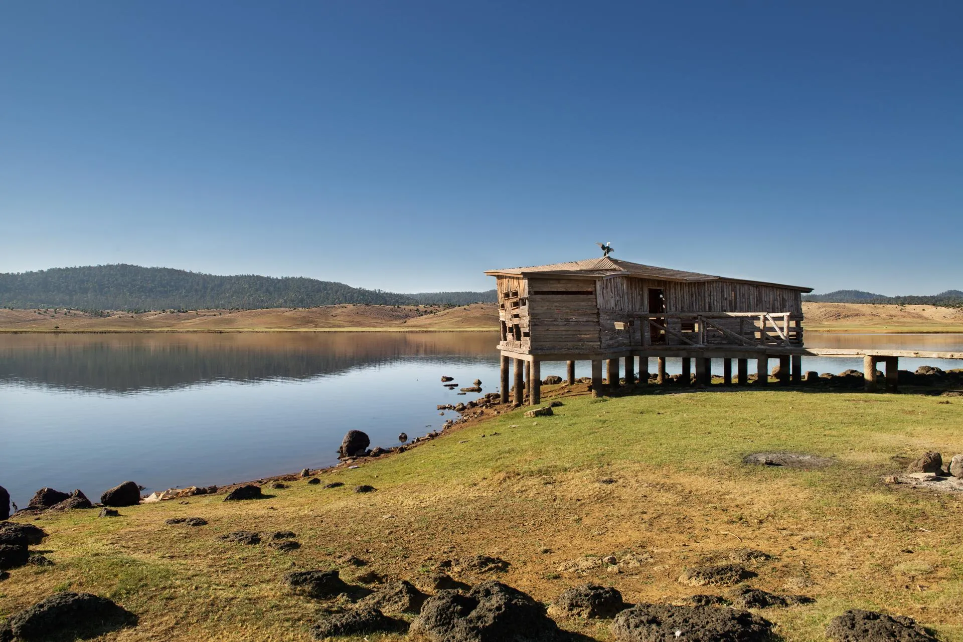 Une cabane en bois sur pilotis au bord d'un lac avec des montagnes en arrière-plan