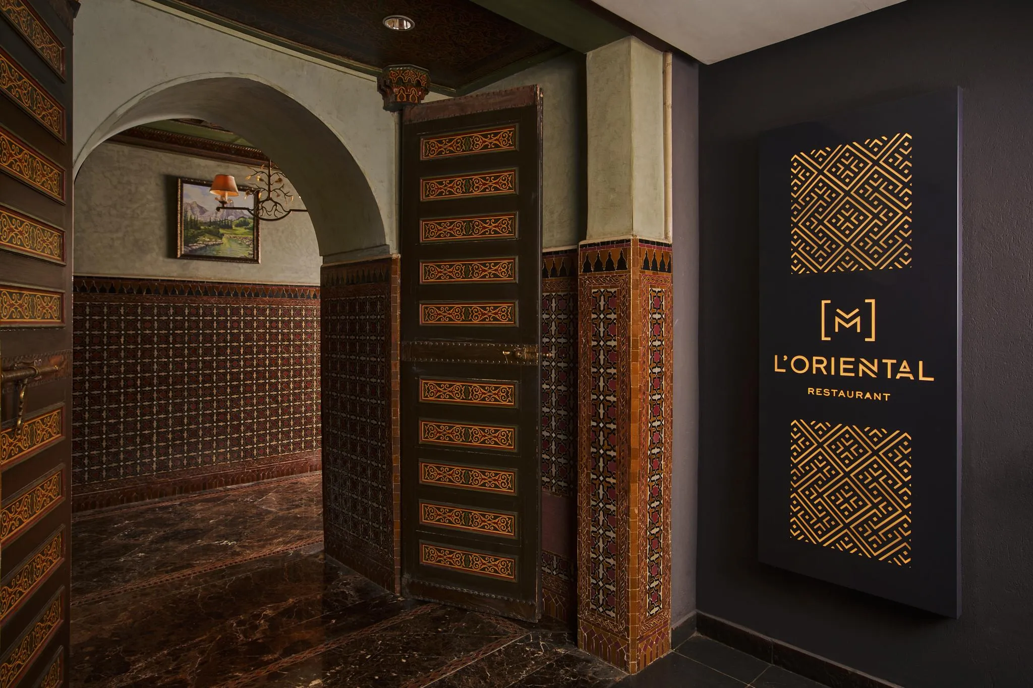 Entrée d'un restaurant nommé L'Oriental avec une porte en bois sculpté et un panneau lumineux à motifs géométriques