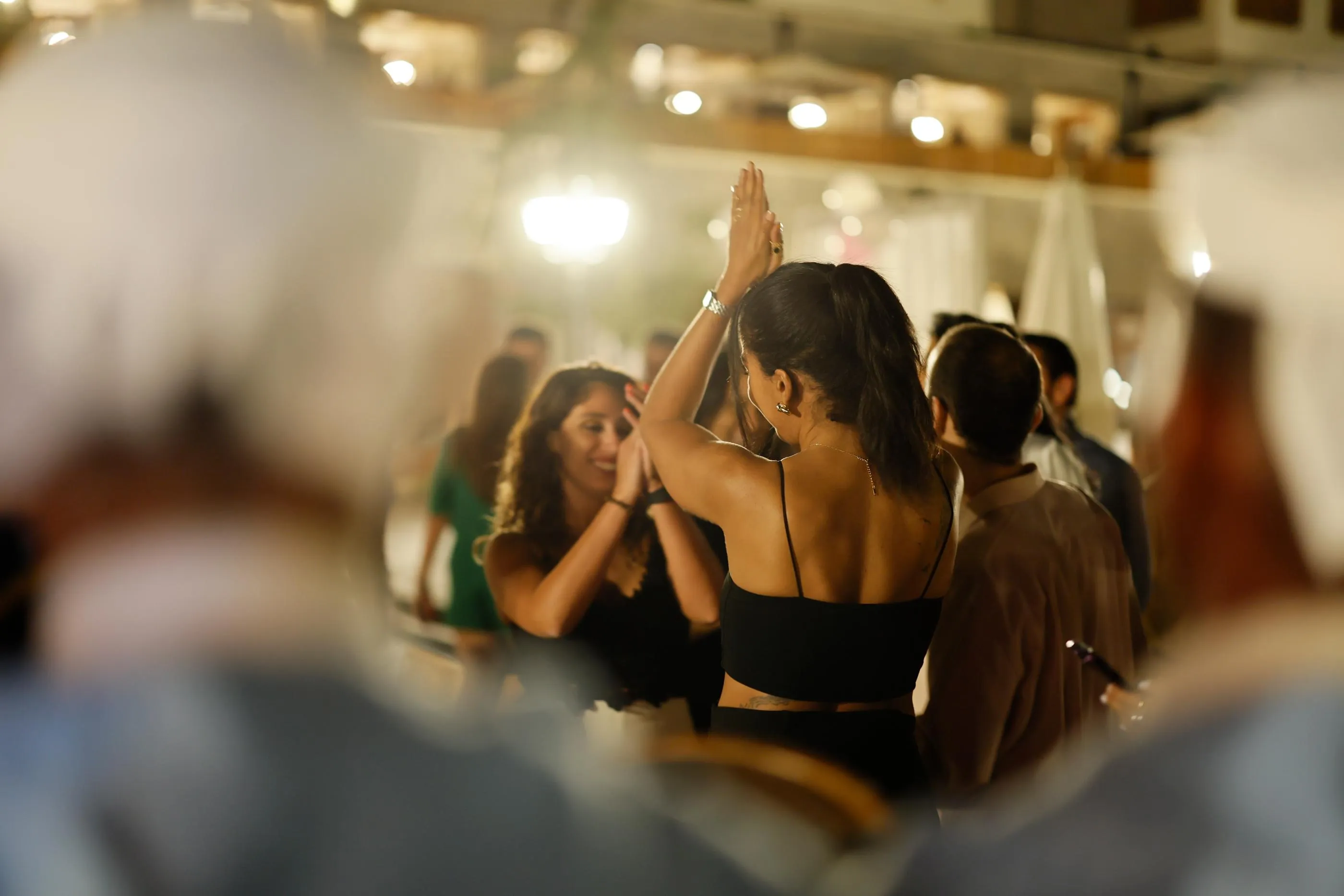 Deux femmes dansent ensemble dans une salle éclairée, entourées d'autres personnes en train de socialiser