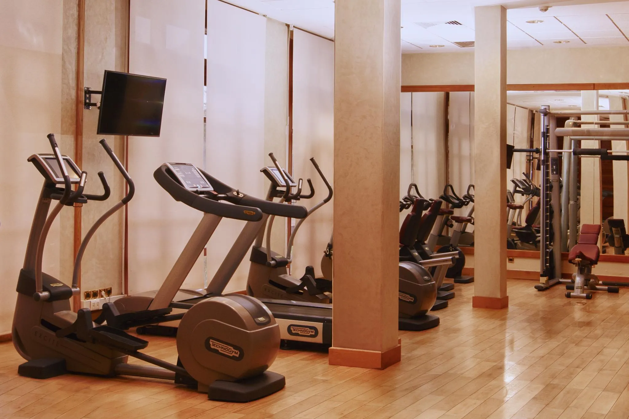 Salle de sport avec plusieurs appareils de cardio-training, dont des elliptiques et des vélos, alignés contre un mur avec des miroirs