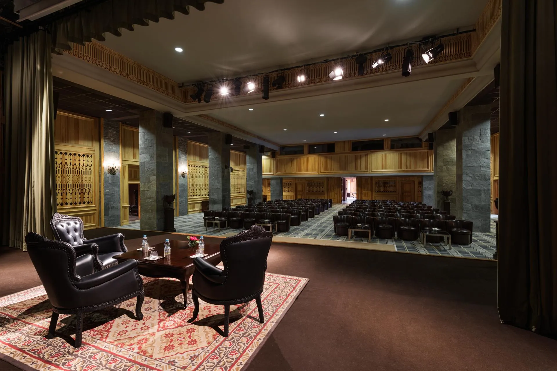 Salle de conférence avec des rangées de chaises et un espace lounge avec deux fauteuils et une table basse