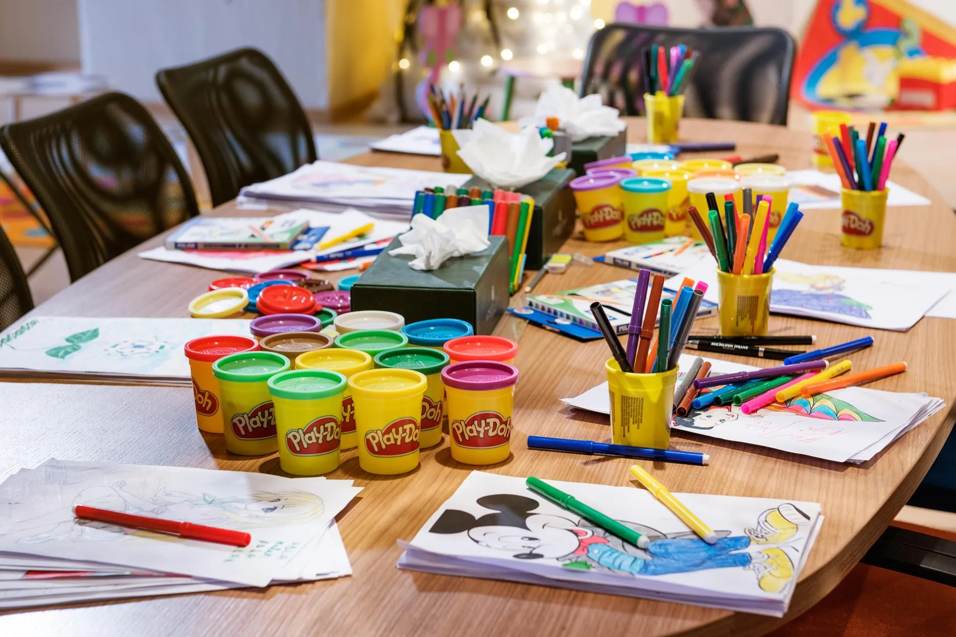 Table avec du matériel de dessin, des pots de pâte à modeler Play-Doh et des feuilles colorées