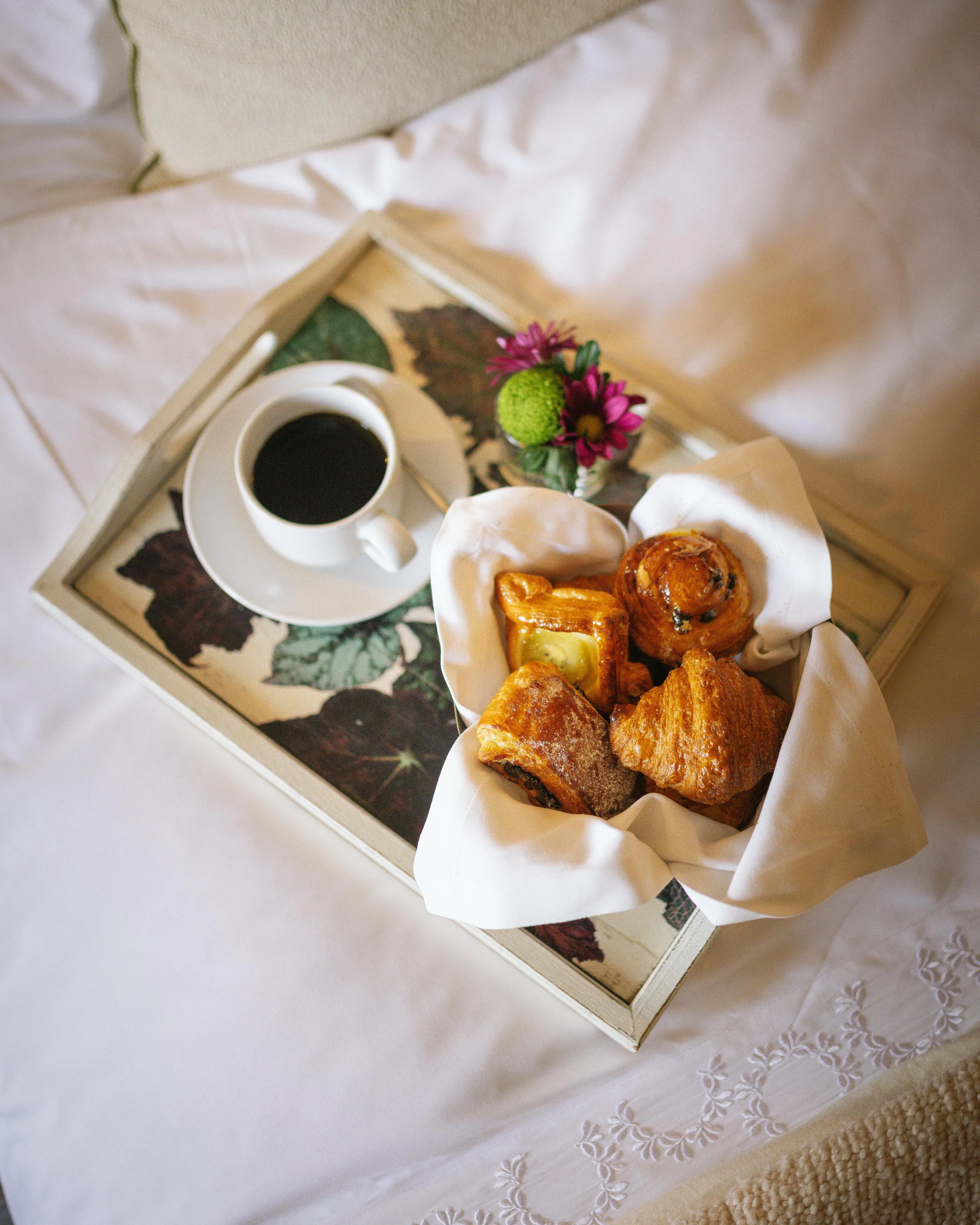 A tray with a cup of coffee, pastries, and flowers on a bed