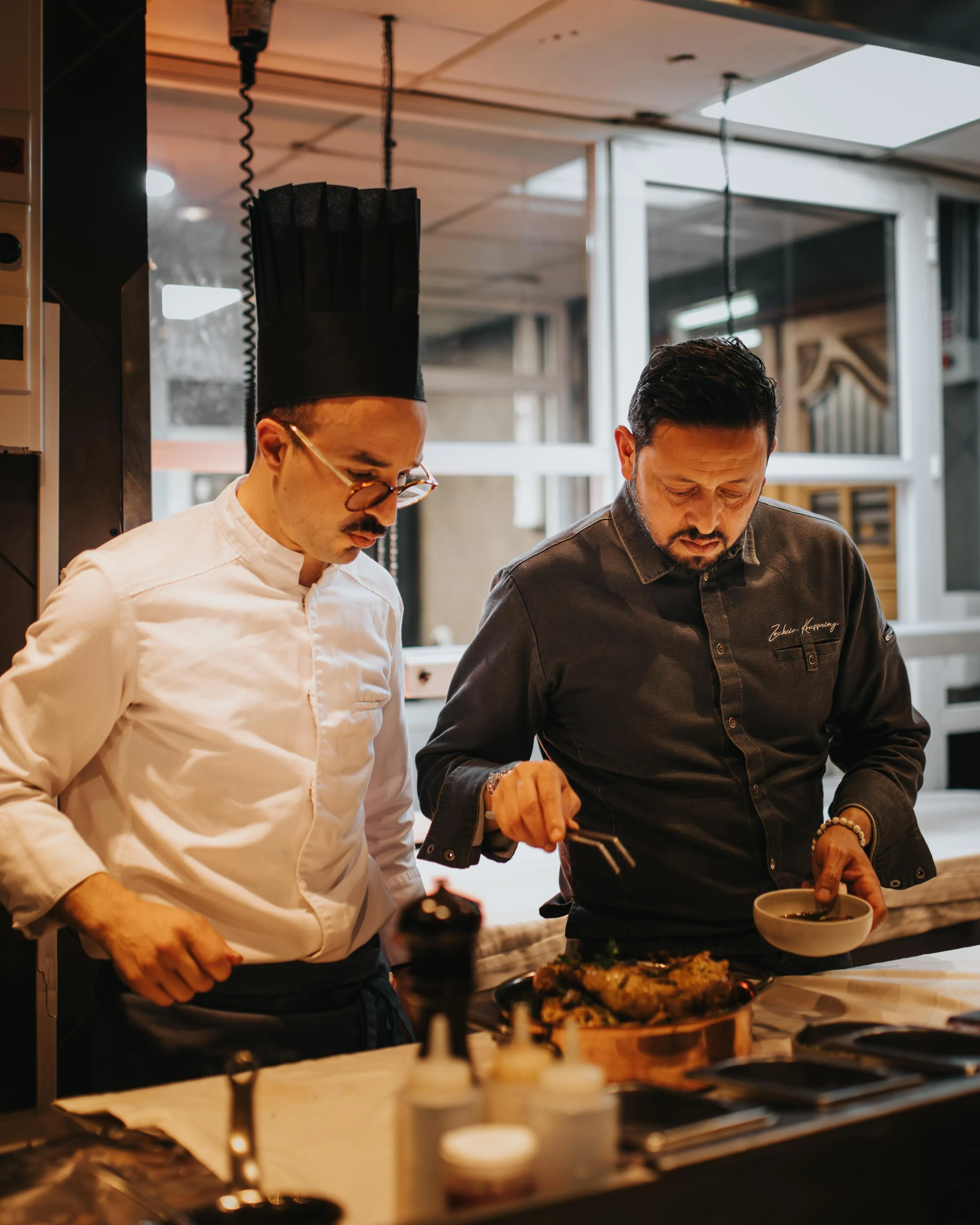 Deux hommes en tenue de cuisine préparent un plat ensemble dans une cuisine professionnelle